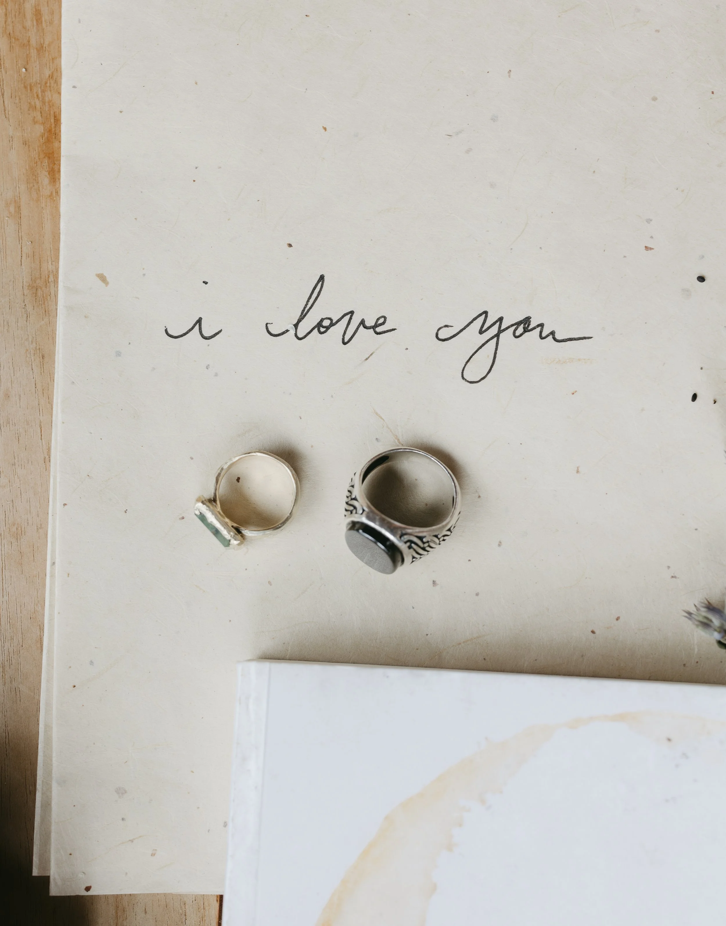 Handwritten note with the words "i love you" on a piece of paper, accompanied by two rings placed underneath the note.