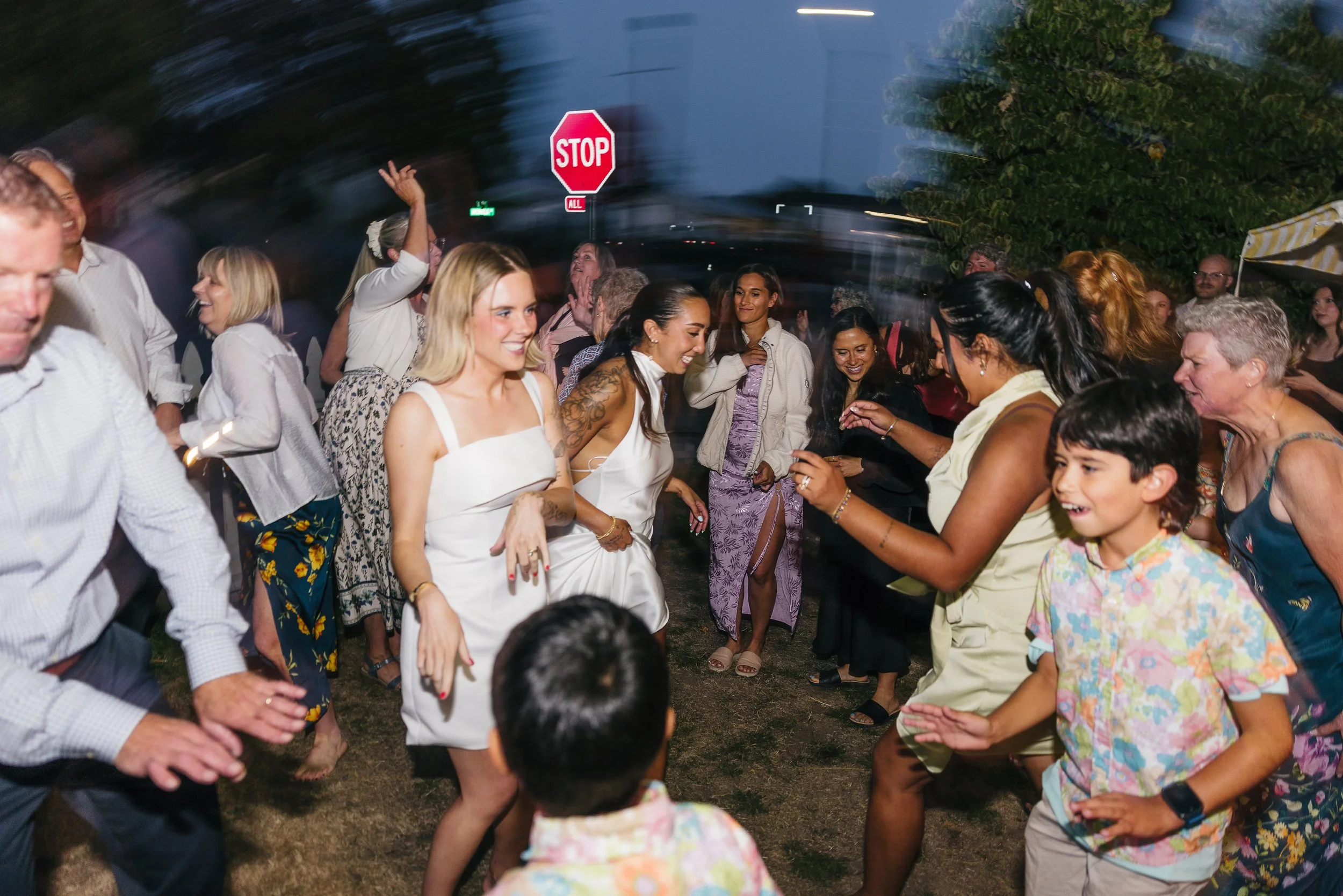 Group of people dancing and enjoying at an outdoor party during the evening, with a stop sign visible in the background.