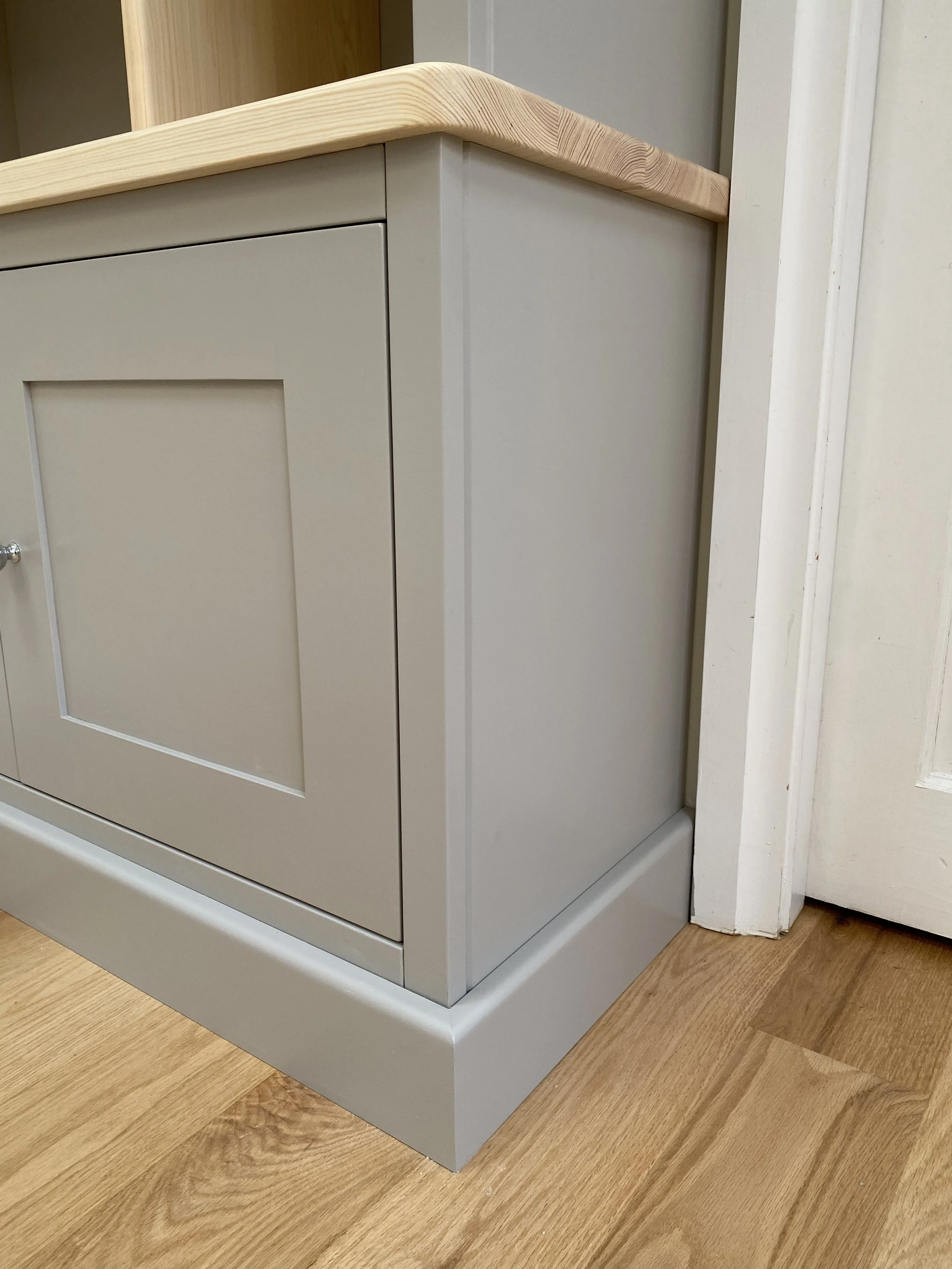 Close-up of a modern kitchen cabinet with beige doors, wooden countertop, and a baseboard on a wooden floor.