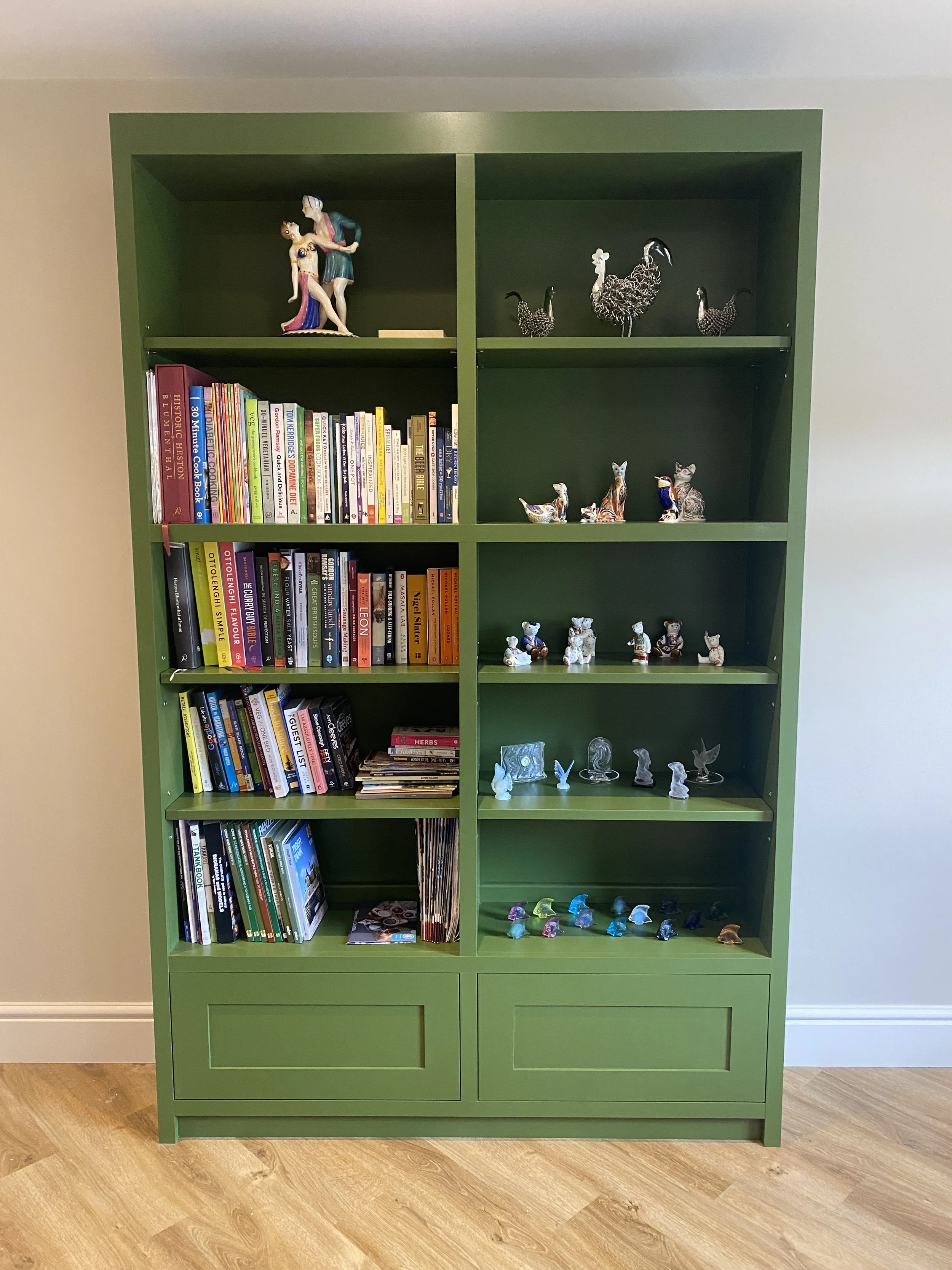 Green bookshelf with books and animal figurines on shelves, and two larger animal figurines on top.
