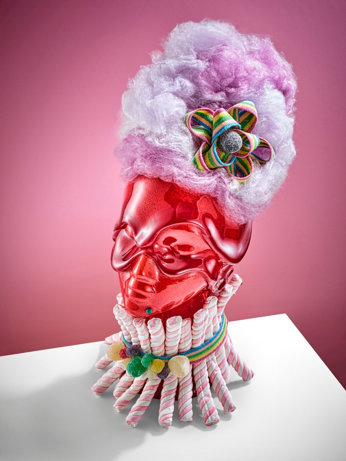Arm Candy by Charlotte Omnes & Marshall Troy - Artistic composition of a red metallic mannequin head with a cotton candy wig and a colorful candy embellishment, set against a pink background.