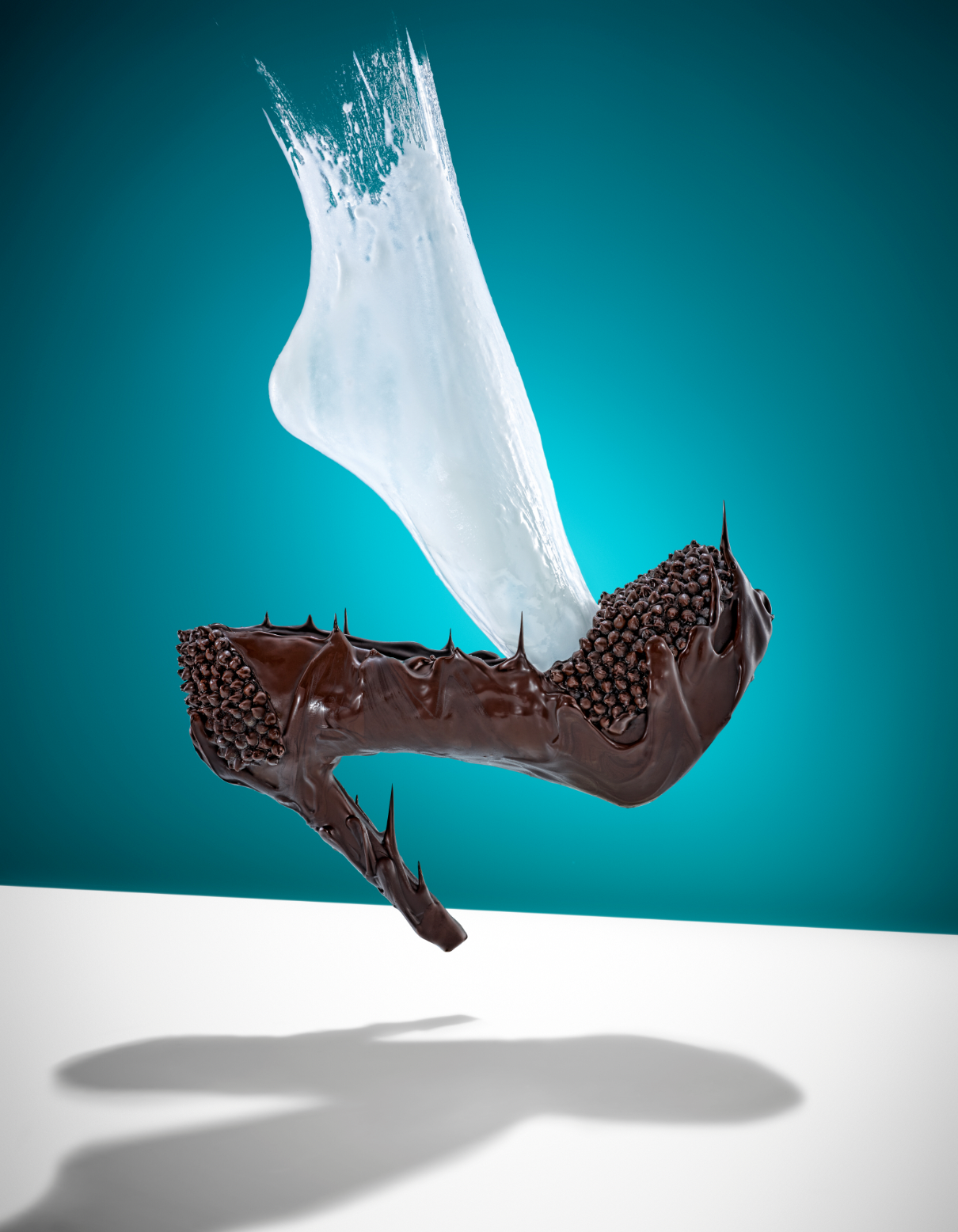 Arm Candy by Charlotte Omnes & Marshall Troy - A high-heeled shoe made of dark chocolate with chocolate sprinkles on a white surface against a blue background. A splash of milk surrounds the shoe.