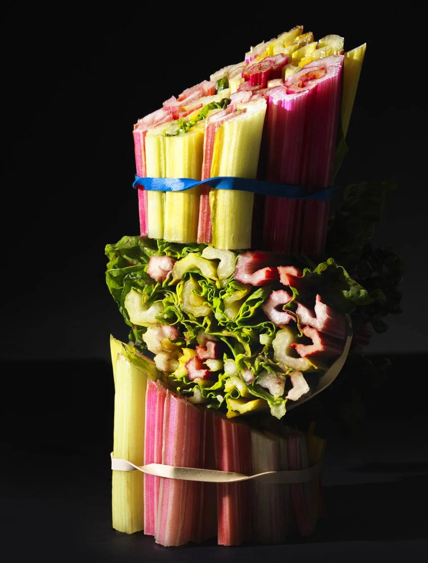 Food Stylist Charlotte Omnes & Photographer Francine Zaslow-Bundles of rainbow chard with colorful stems tied with rubber bands, displayed vertically against a dark background.