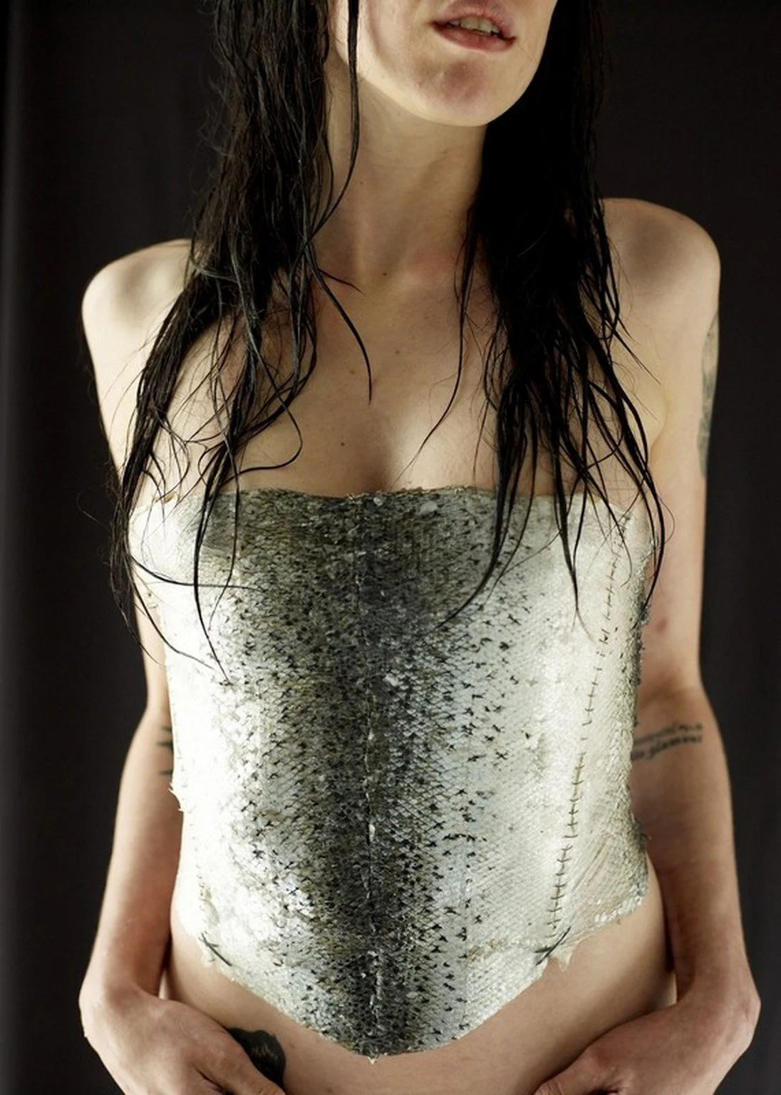 Person wearing a fish skin bodice, with wet hair, tattoos visible on arms. By Charlotte Omnes