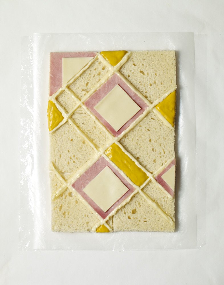Food Stylist Charlotte Omnes & Photographer Beth Galton-Artistic sandwich with layers of bread, cheese, and ham arranged geometrically with mustard and mayonnaise accents on parchment paper.