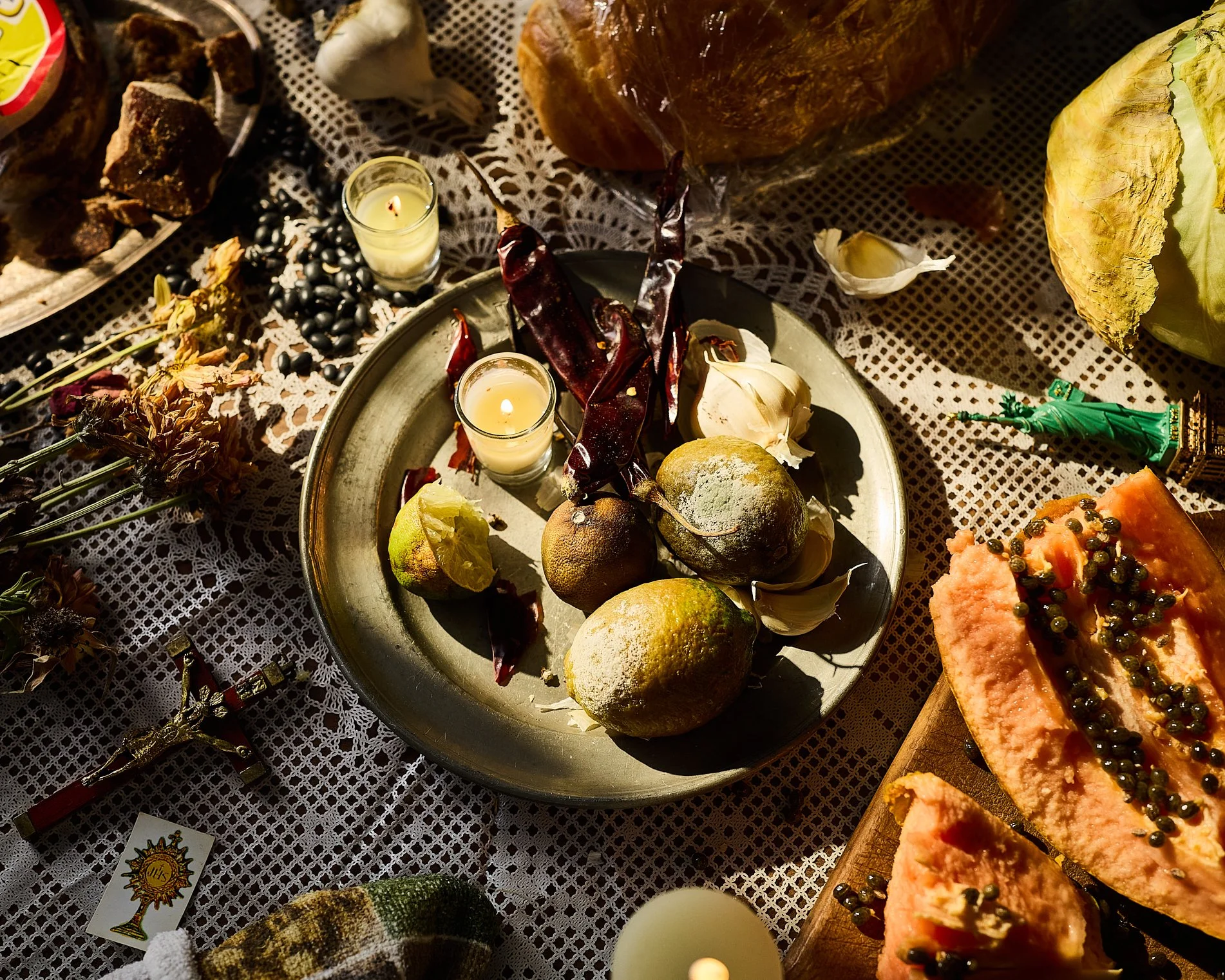 A table with a lace tablecloth decorated with food, candles, flowers, and religious figures, including roasted meat, bread, and pastries, suggestive of a festive or religious celebration.