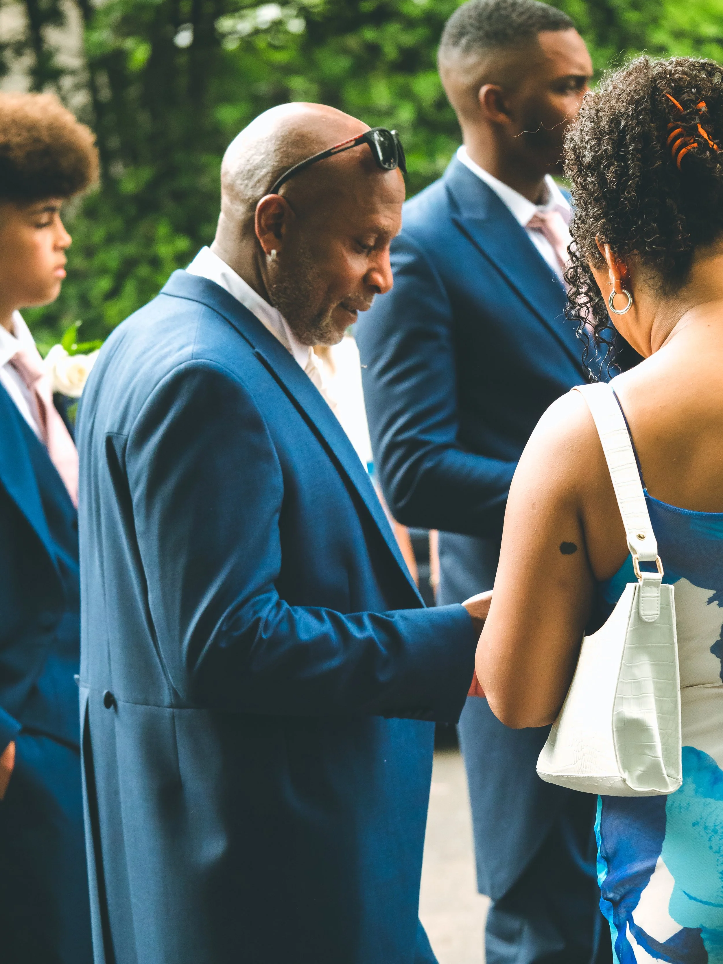 Close-up of a group of people in formal attire participating in a ceremonial event outdoors, with greenery in the background.