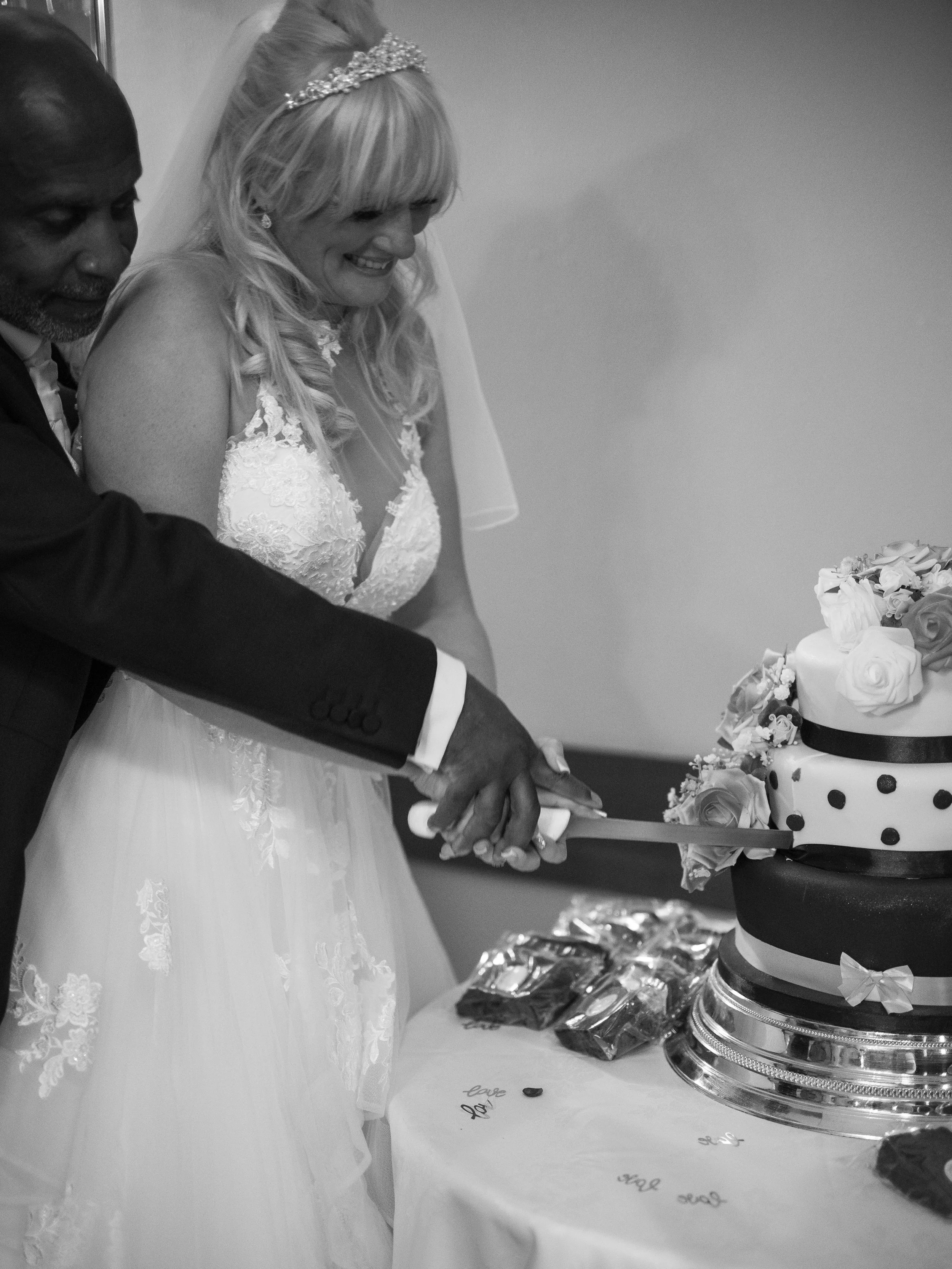 A bride and groom holding hands during their wedding cake cutting ceremony, with a decorated tiered cake on the table.