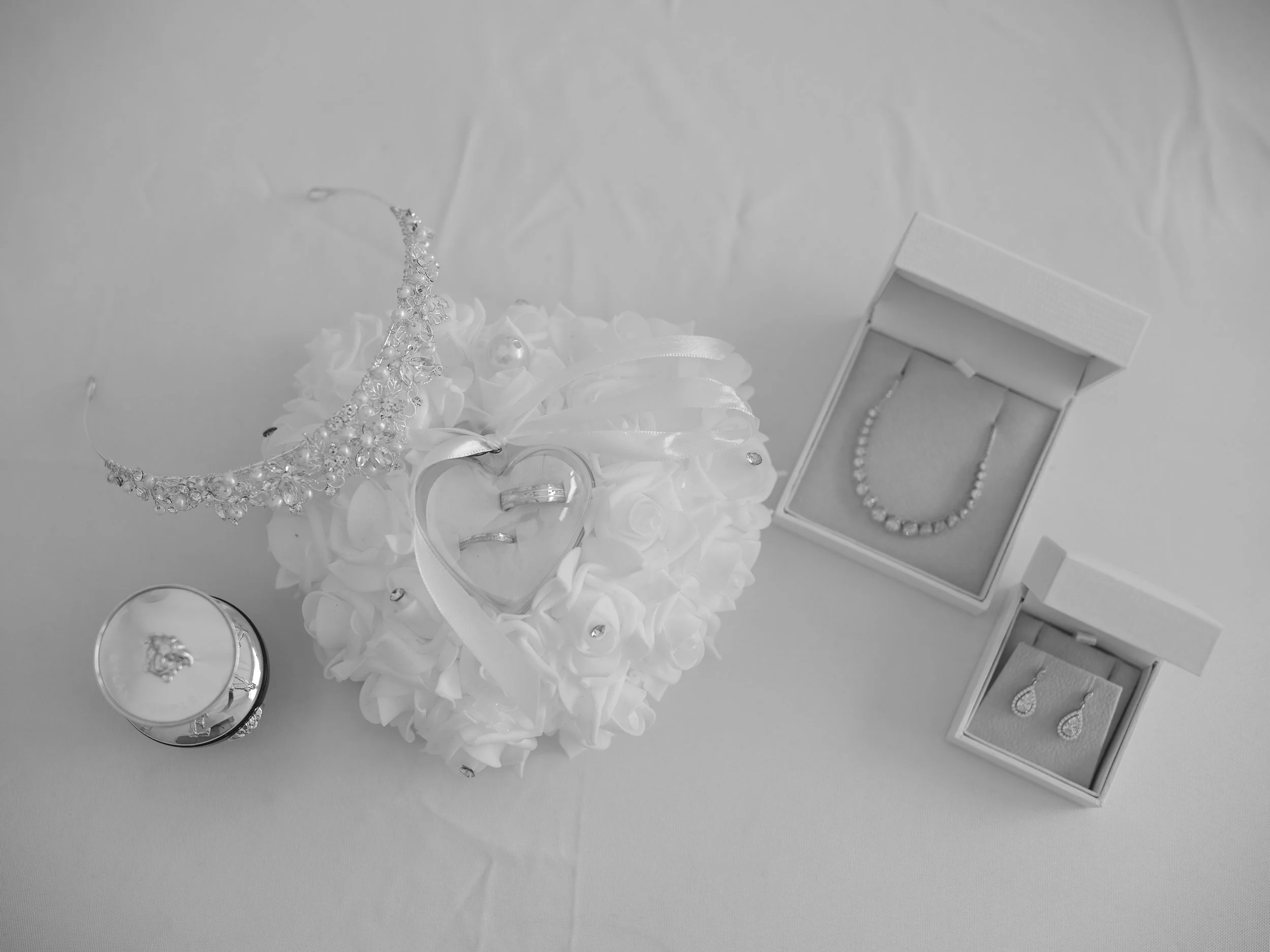 A collection of jewelry including a tiara, rings, earrings, and a necklace, displayed with a bouquet of white flowers and a jewelry box on a white surface.