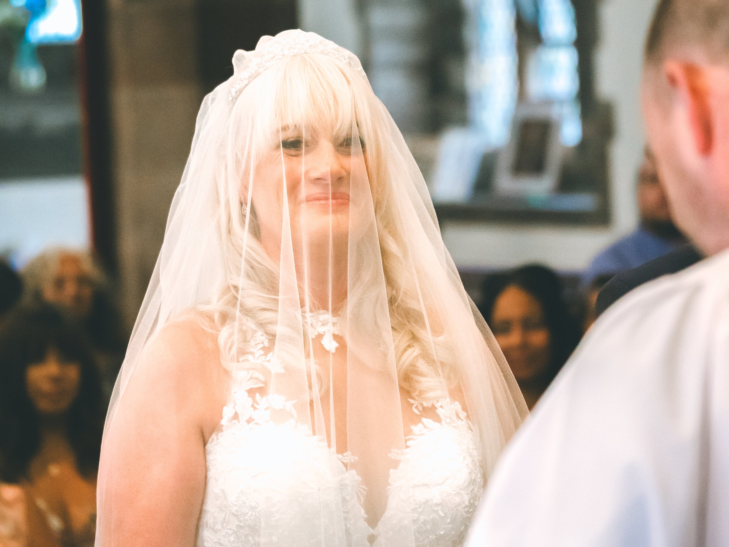 A bride with blonde hair in a wedding dress and veil, smiling during her wedding ceremony.