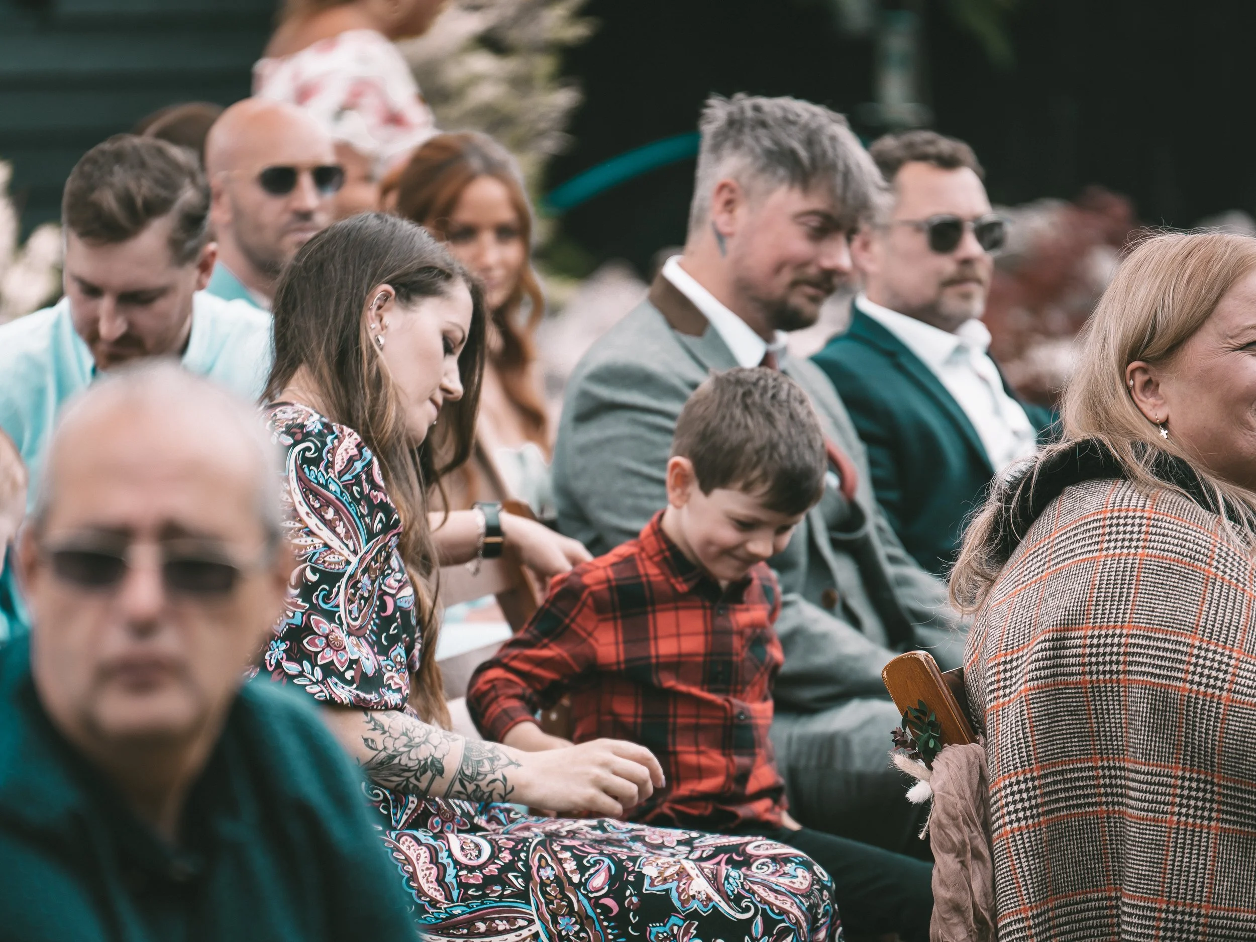 A group of people seated outdoors, dressed in formal and casual attire, participating in an event or gathering.