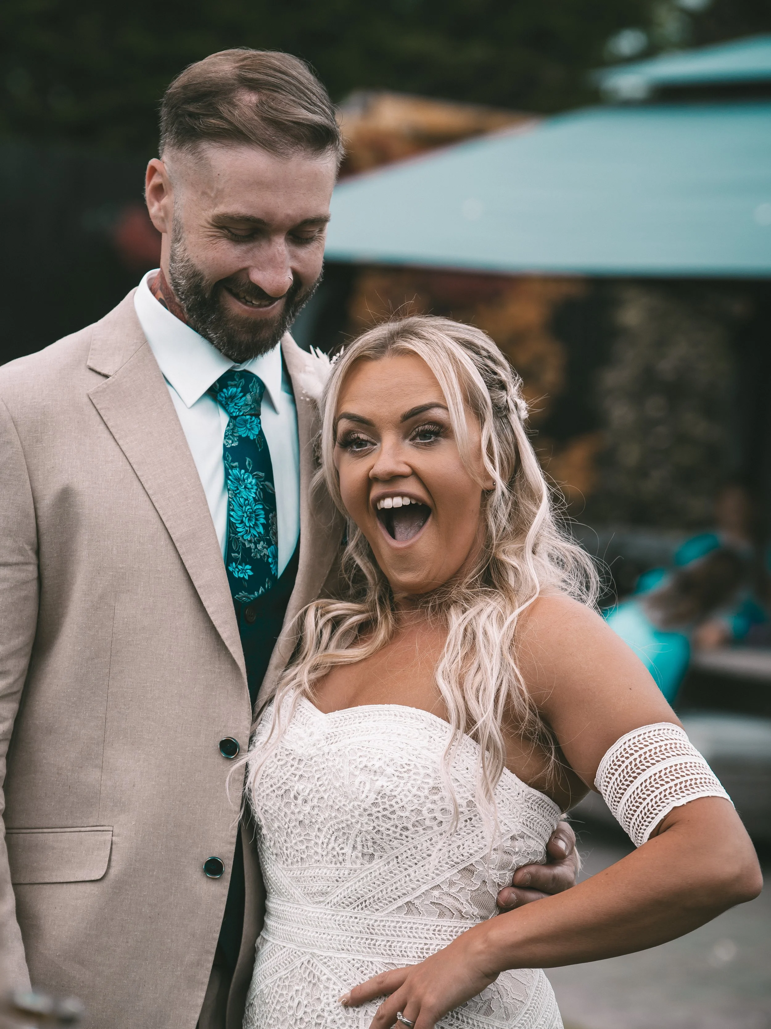 A couple, dressed in wedding attire, smiling and sharing a moment outdoors.