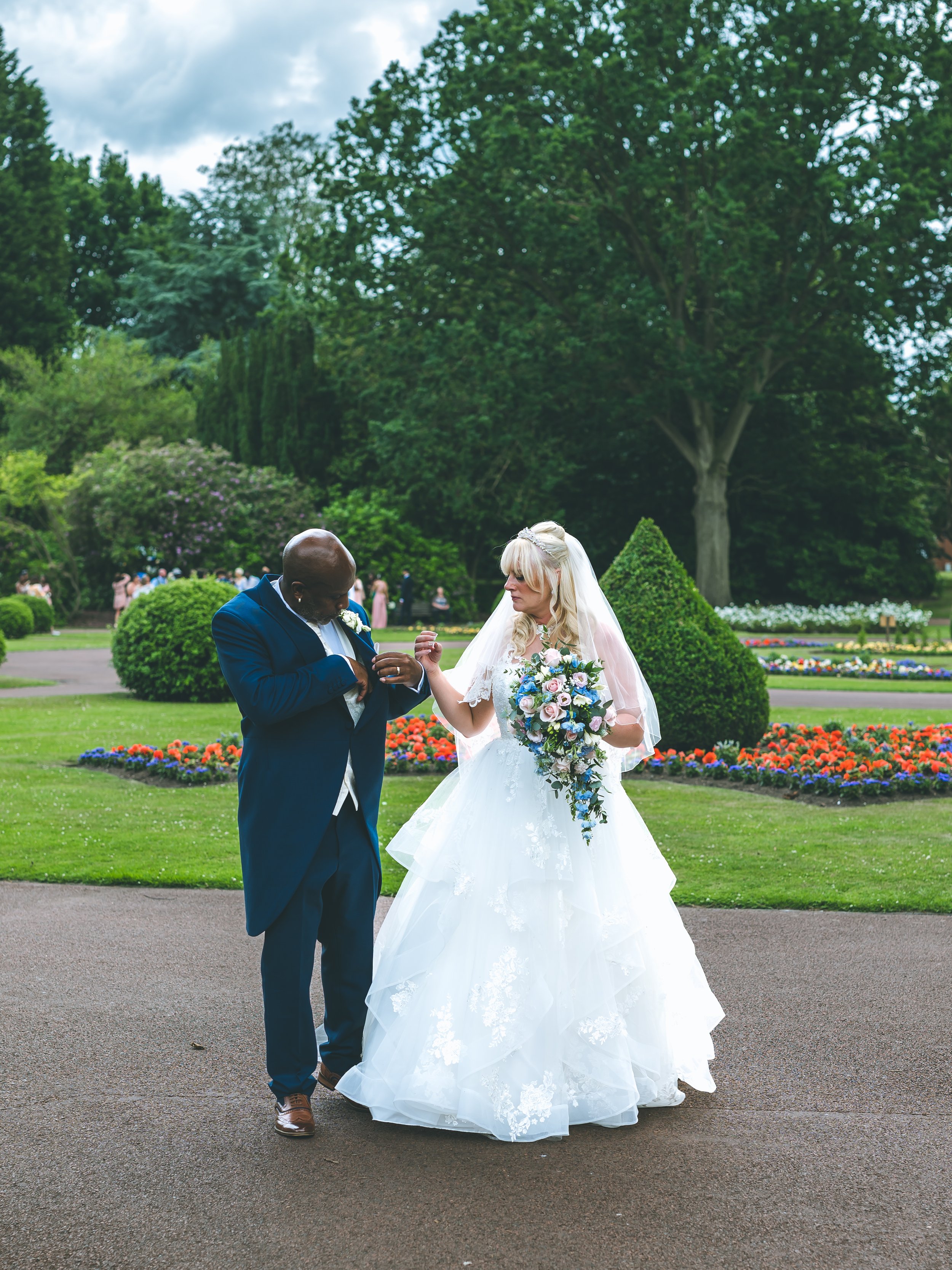 A bride and groom sharing a moment in a garden during a wedding ceremony, with colorful flowers and green trees in the background.