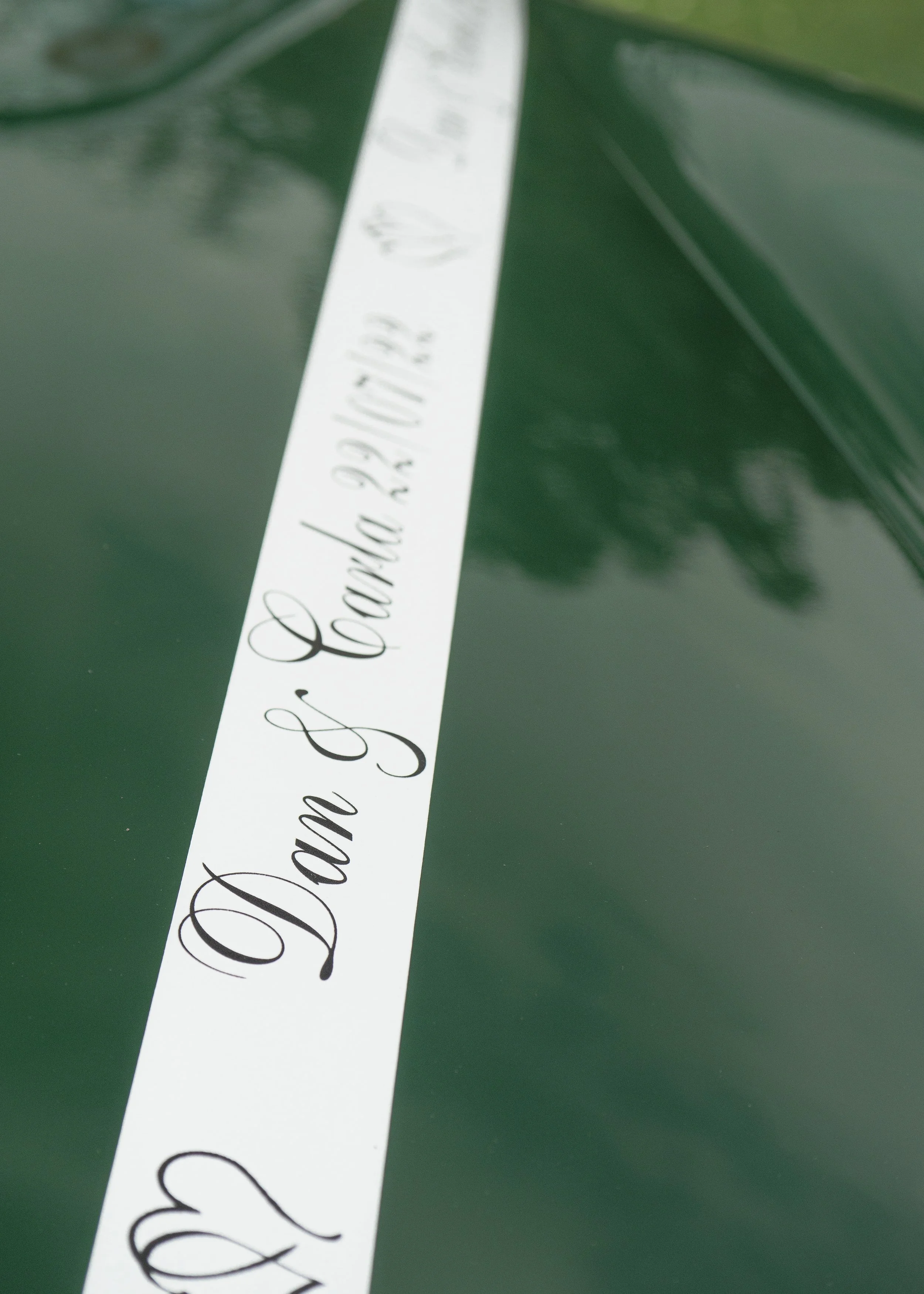 A close-up of a white ribbon with black cursive text on a dark green background.