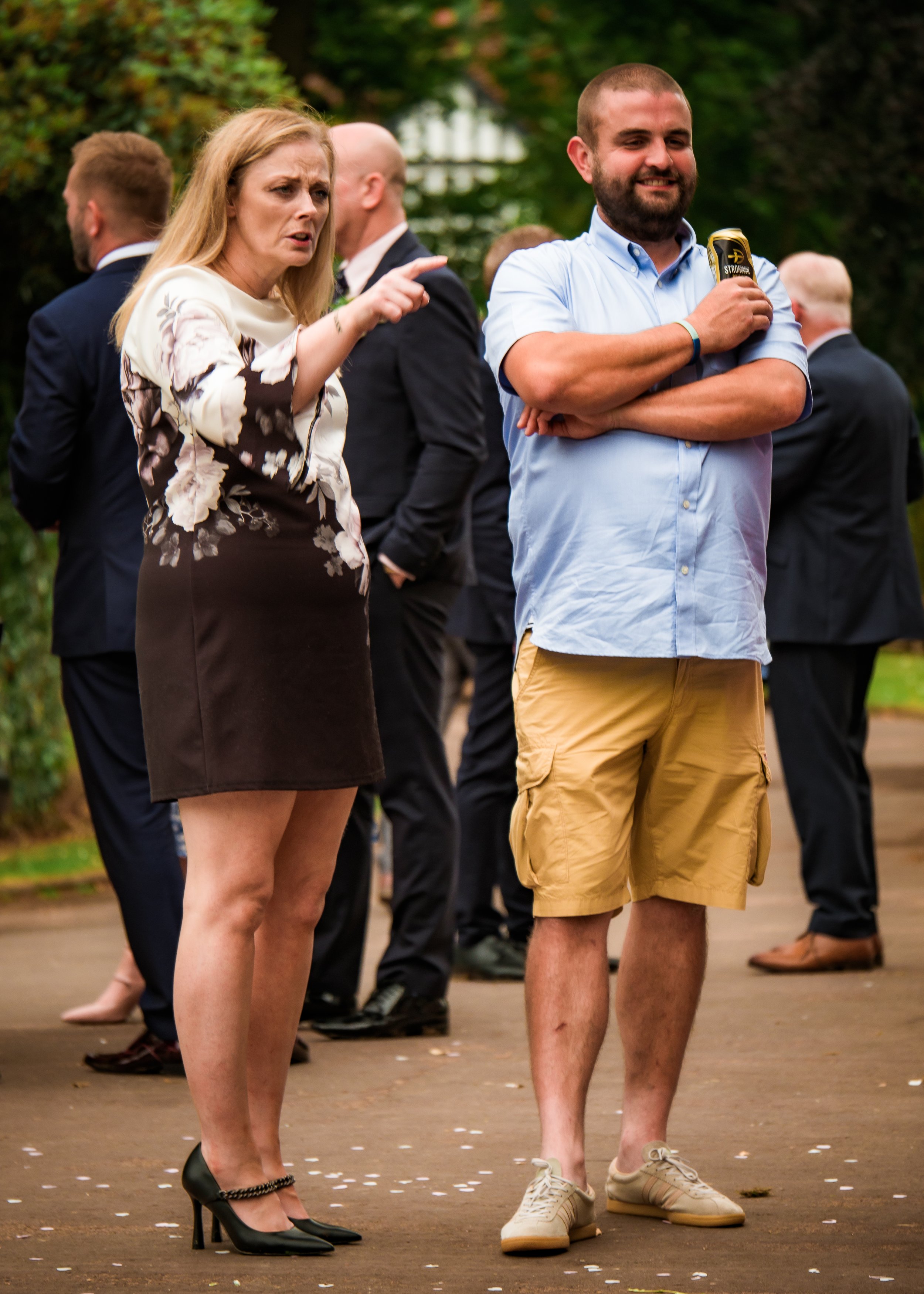 People standing outdoors, engaged in conversation at an event, with trees in the background.