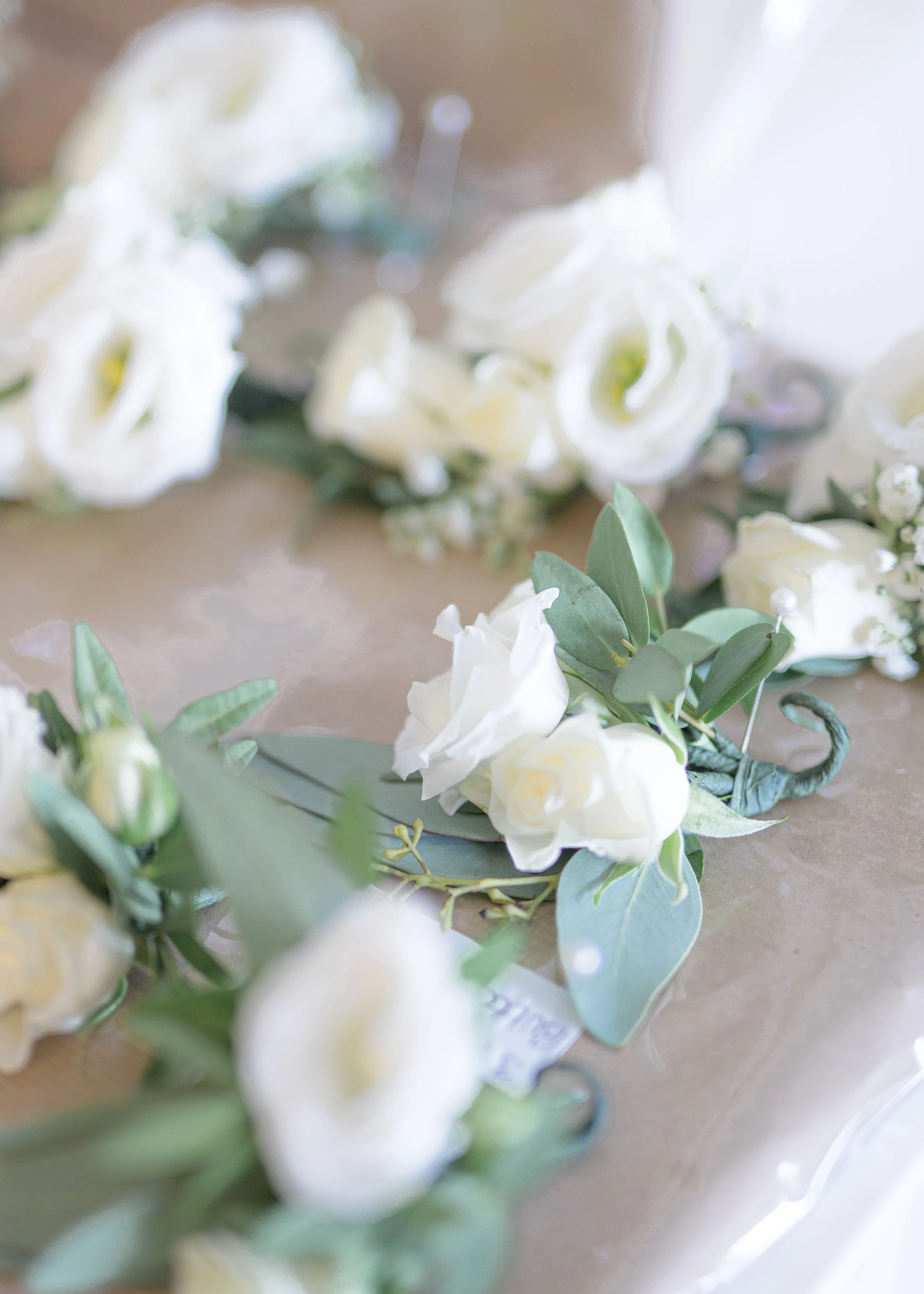 Close-up of a floral arrangement with white roses, green eucalyptus leaves, and small white buds, on a beige surface.