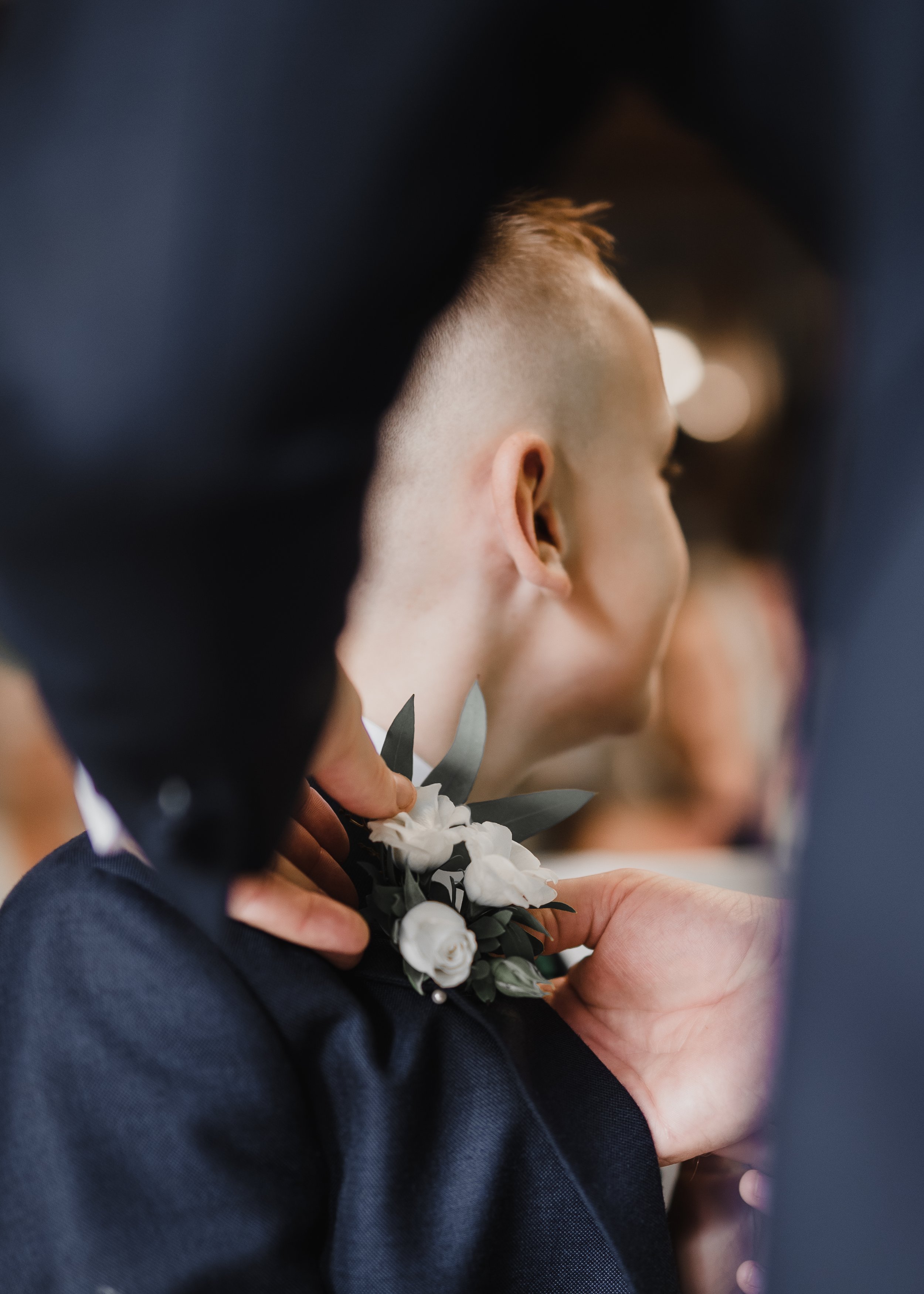 A person with a low fade hairstyle is holding white flowers, possibly at a formal event. The image is taken from the side and focus is on the person's head and hand.