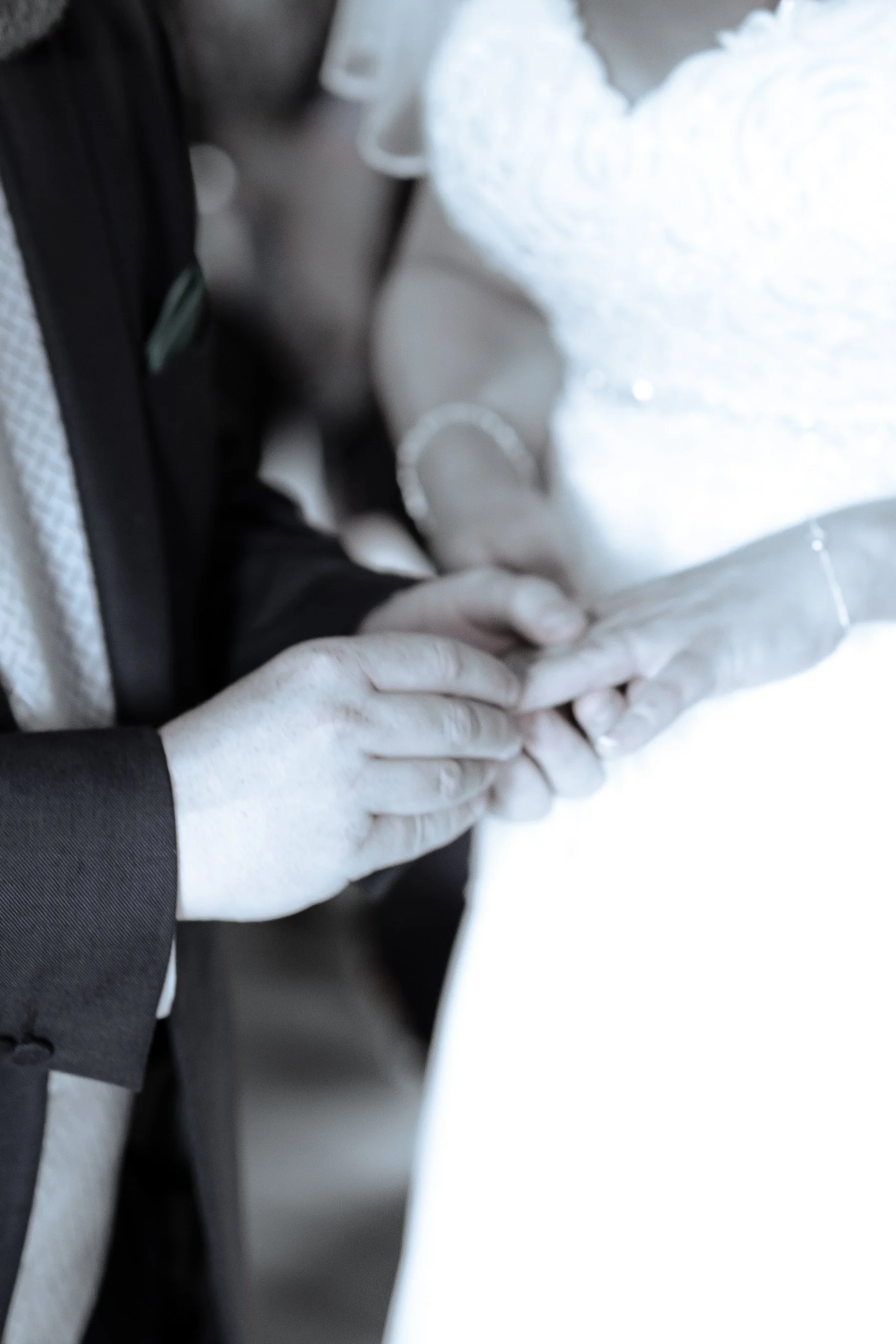 Close-up of hands wearing white gloves holding a white object, possibly a medical or scientific instrument, near a white surface with a person in dark clothing visible in the background.