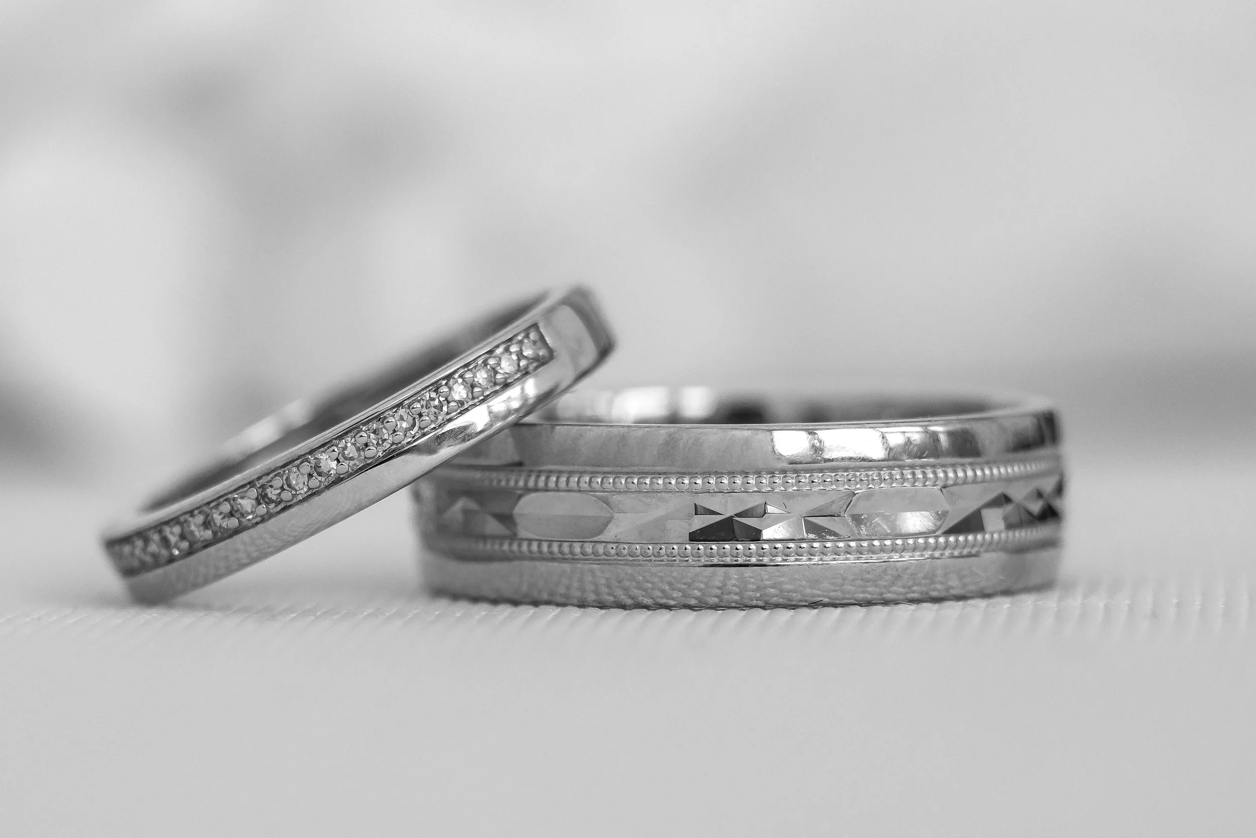 Close-up of three silver rings with decorative patterns, one featuring small gemstones, placed on a white surface.