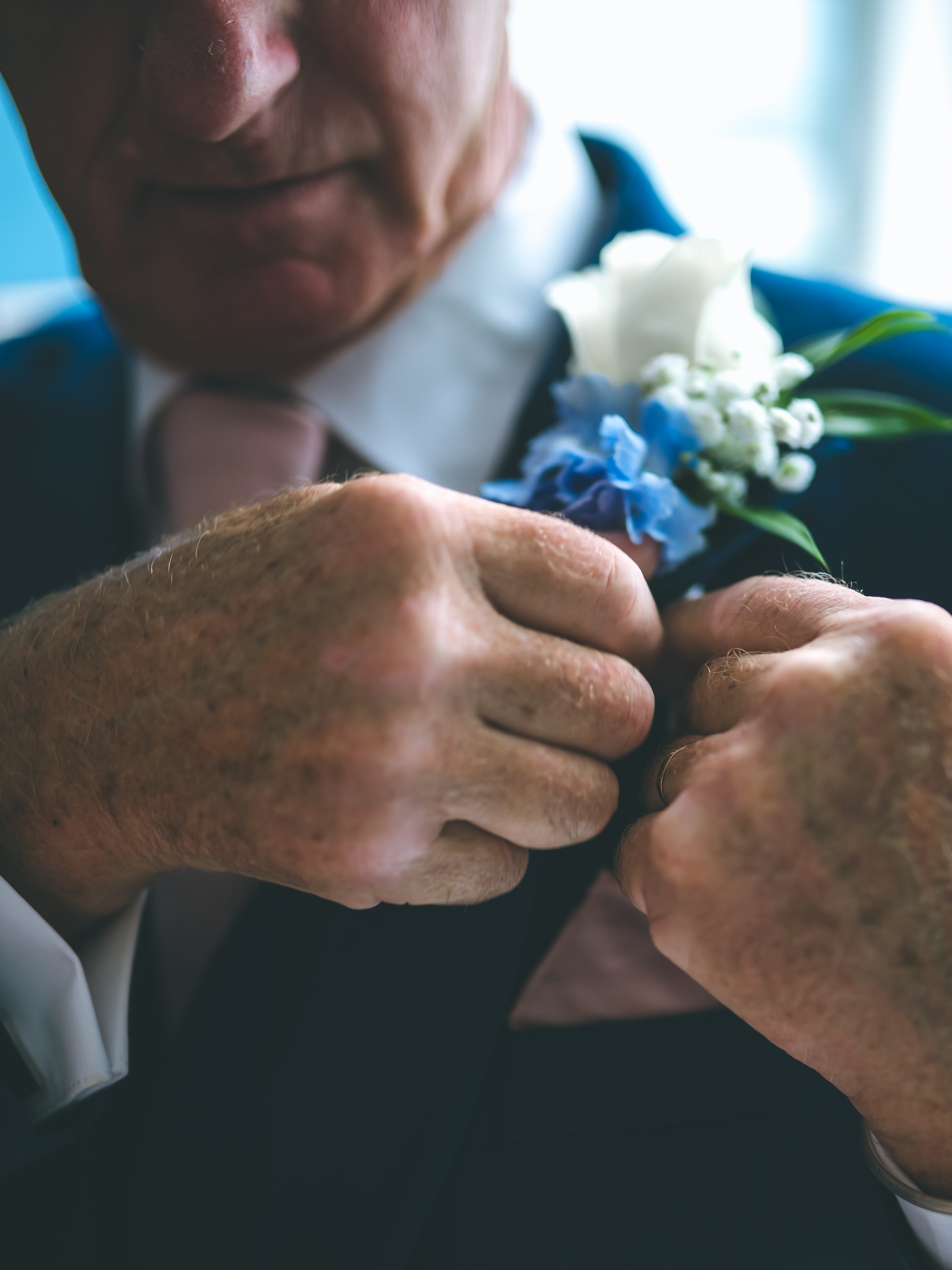 Close-up of an elderly person's hands holding a small bouquet of white and blue flowers.