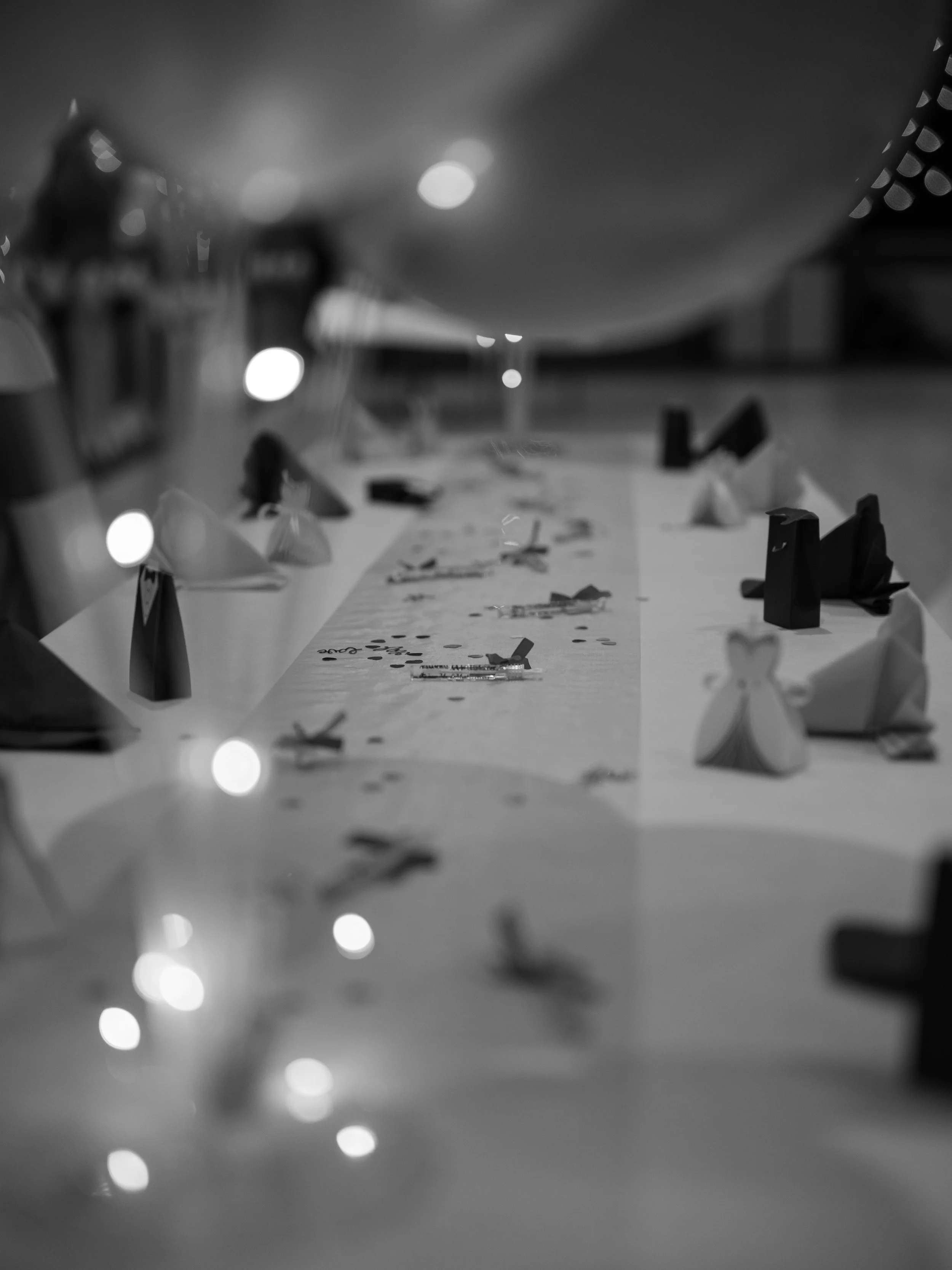 Blurred black and white photo of a decorated table with party hats, confetti, snacks, and a large balloon overhead
