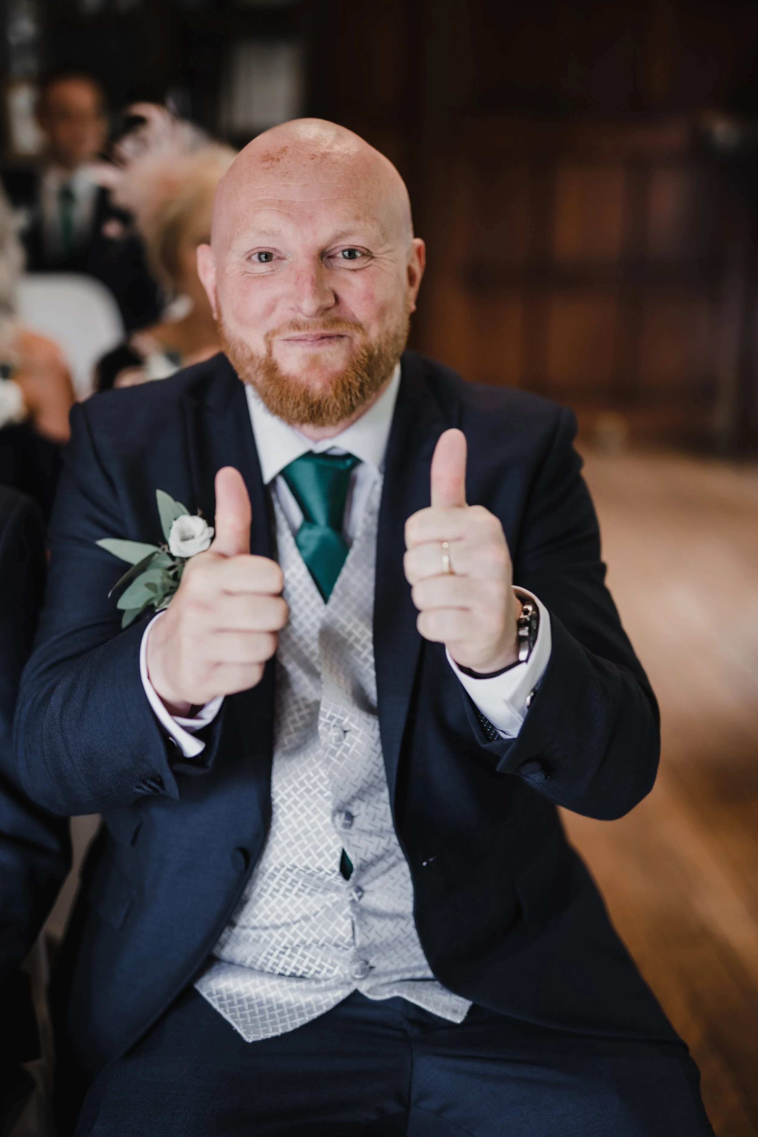 Man with a red beard and bald head giving a thumbs-up gesture at a formal event.