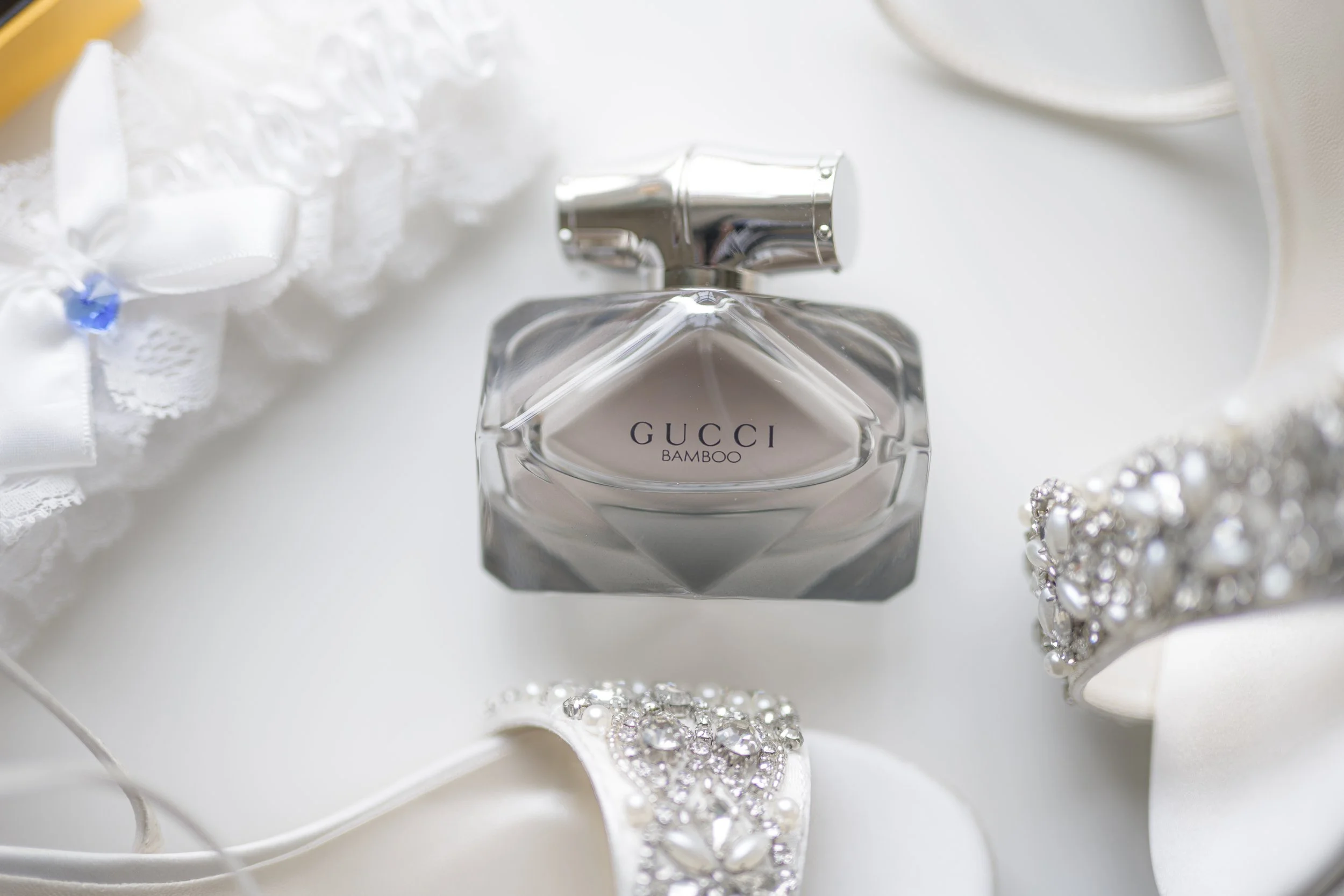 A bottle of Gucci Bamboo perfume next to jewelry and lace accessories on a white surface.