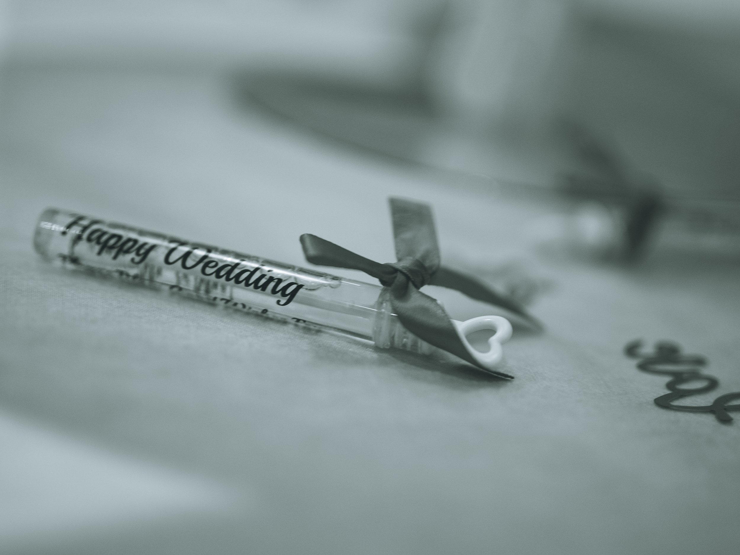 Close-up of a silver wedding ring with the engraved message 'Happy Wedd...' and a black ribbon, placed on white paper with cursive writing.