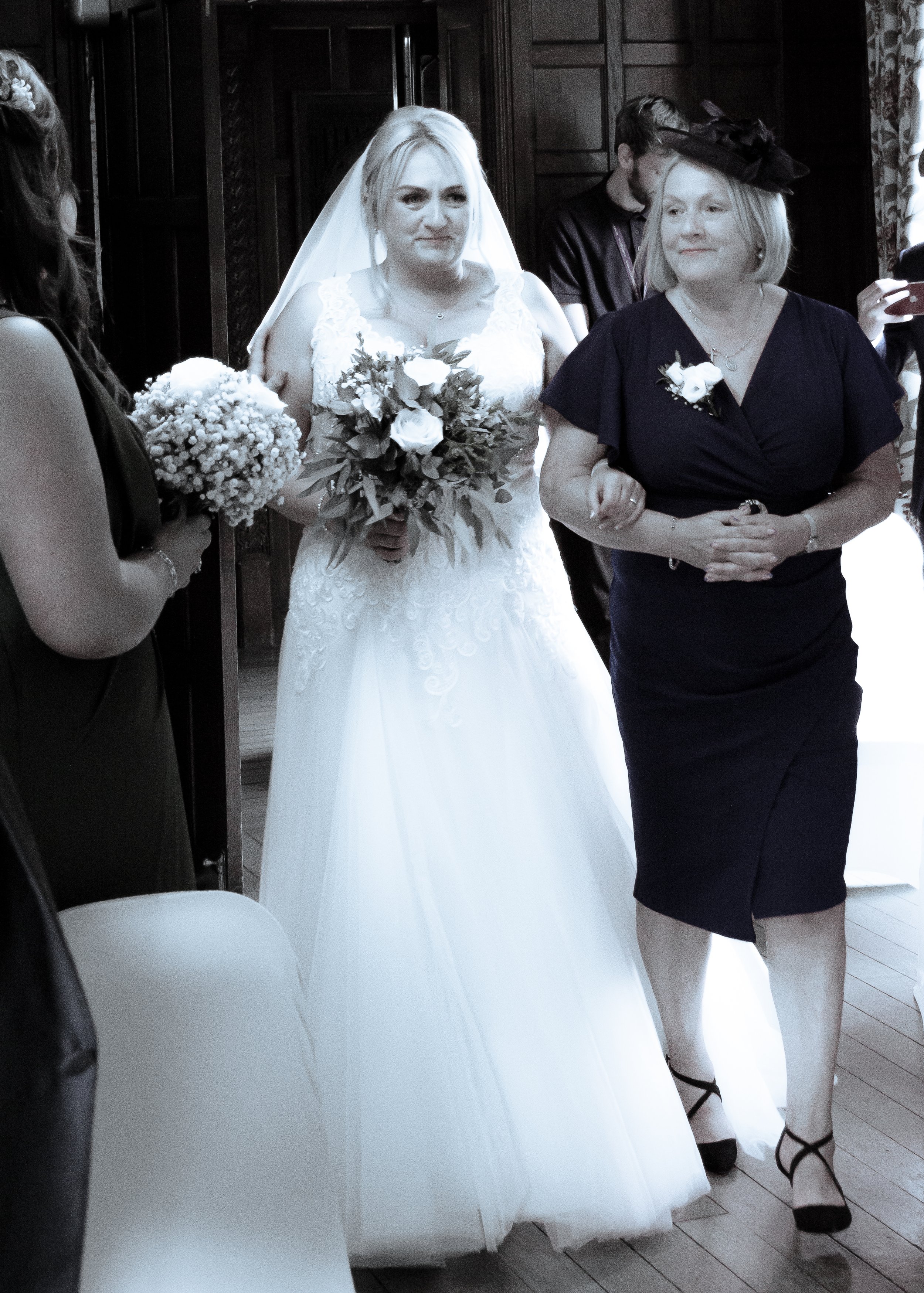 A bride in a white wedding dress holding a bouquet of flowers standing between women at her wedding.