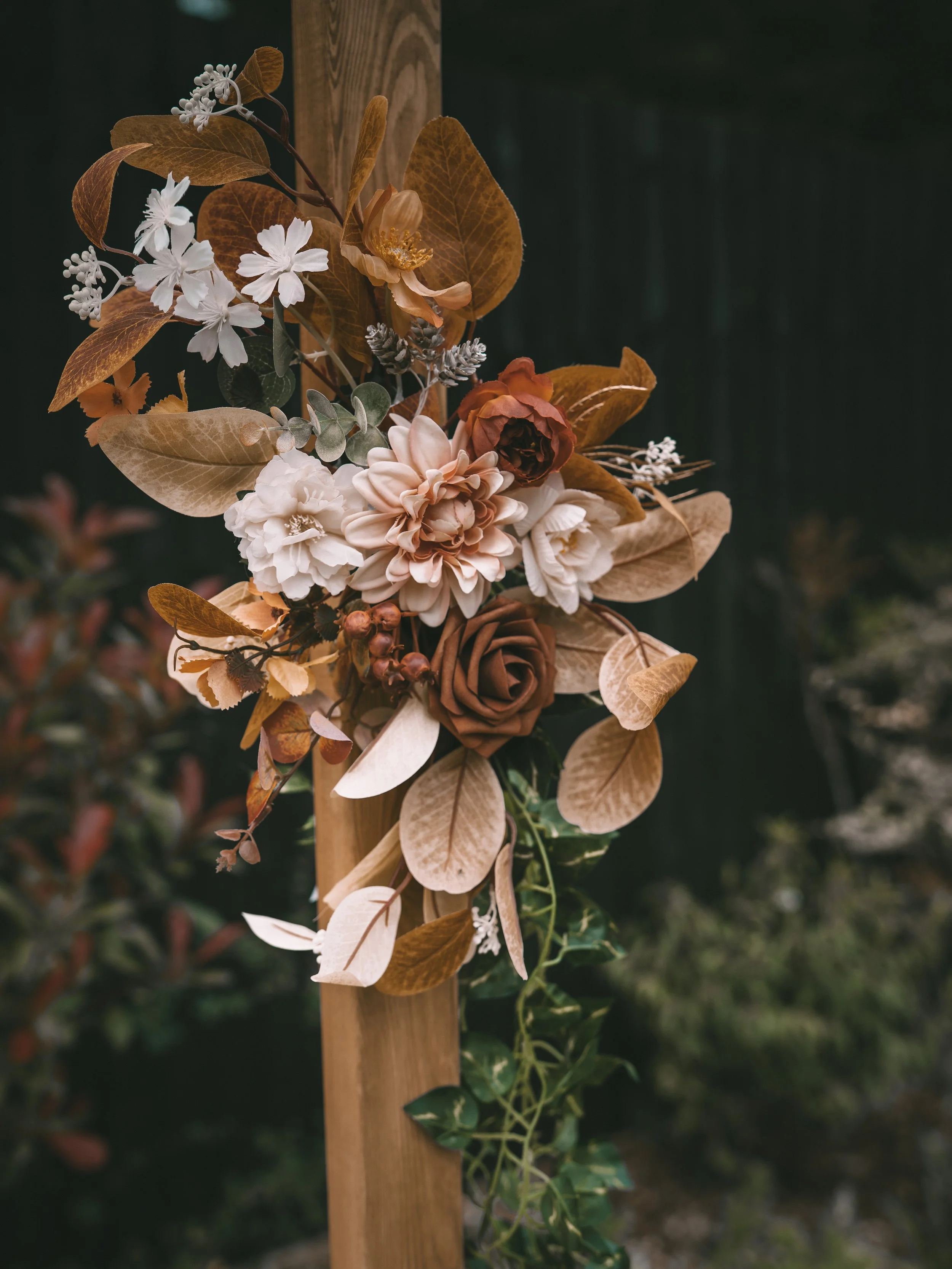 Decorative floral arrangement attached to a wooden stake, featuring white, beige, and brown flowers with assorted leaves.