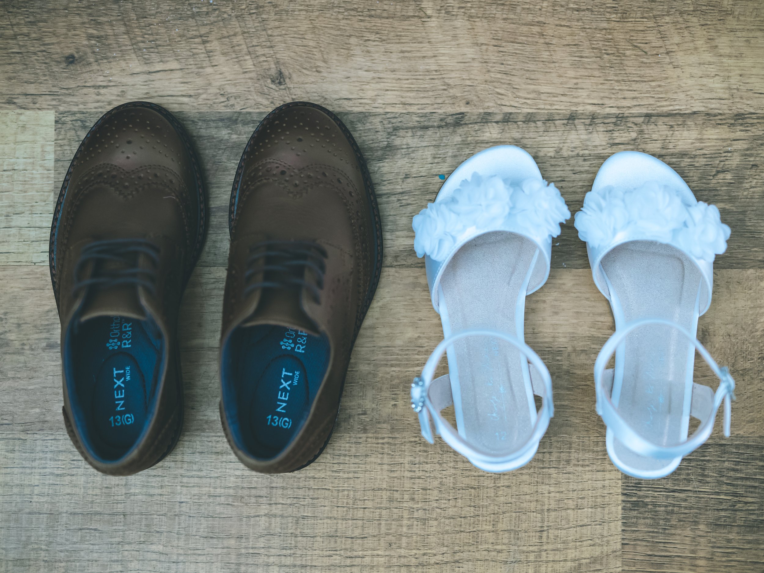 A pair of brown leather dress shoes and a pair of white slippers with fluffy trim on a wooden floor.