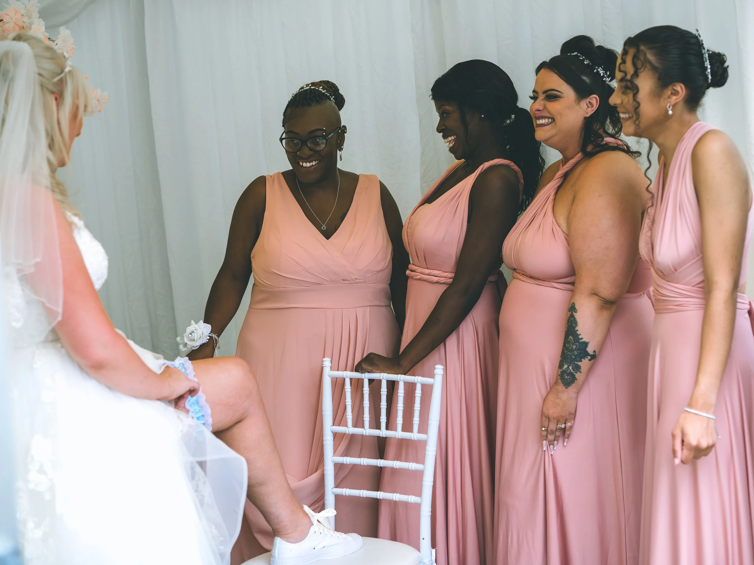 Group of women dressed in pink bridesmaid dresses smiling and standing in a line at a wedding ceremony.