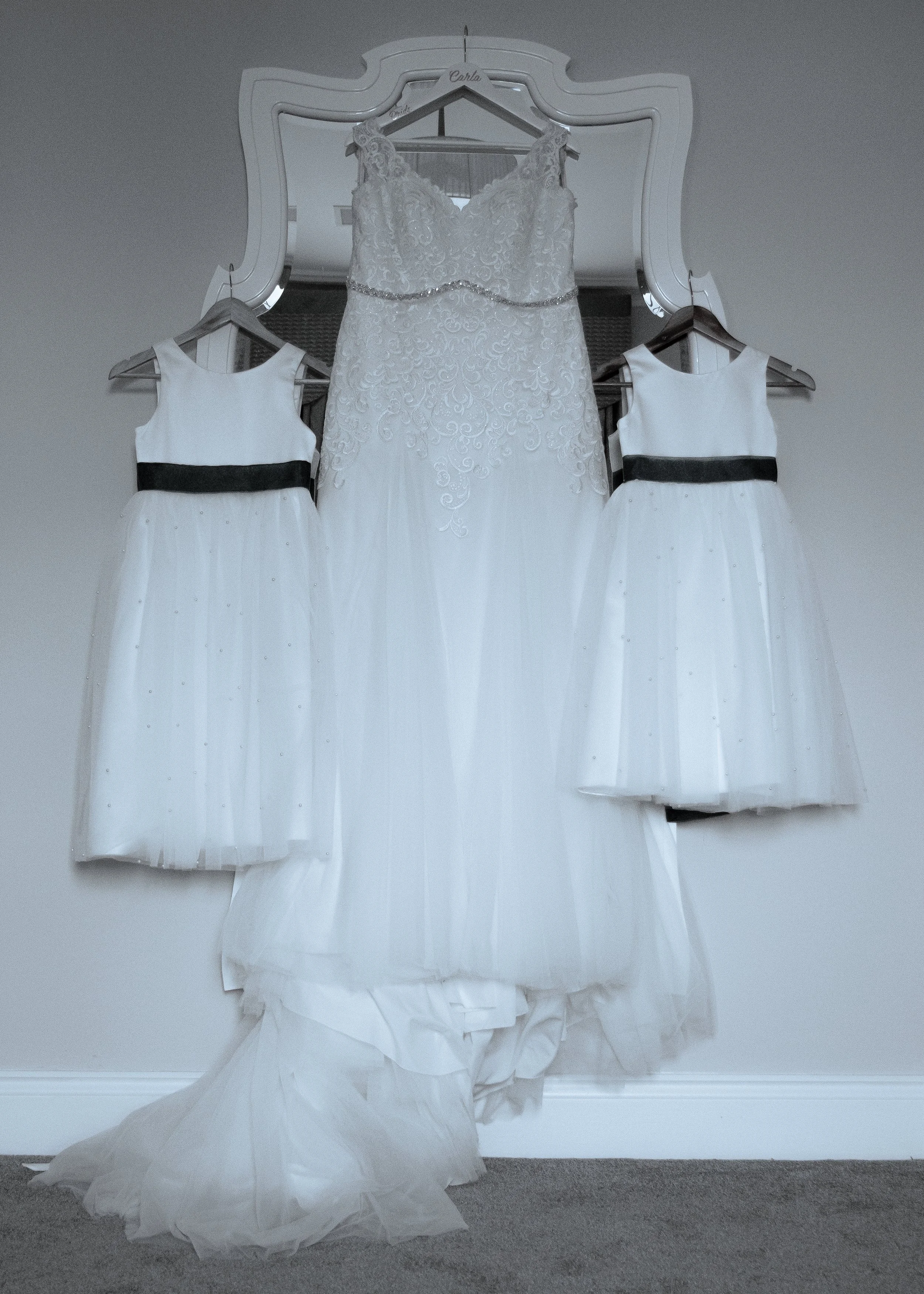 A white wedding dress hanging on a mirror with two smaller white dresses on either side.