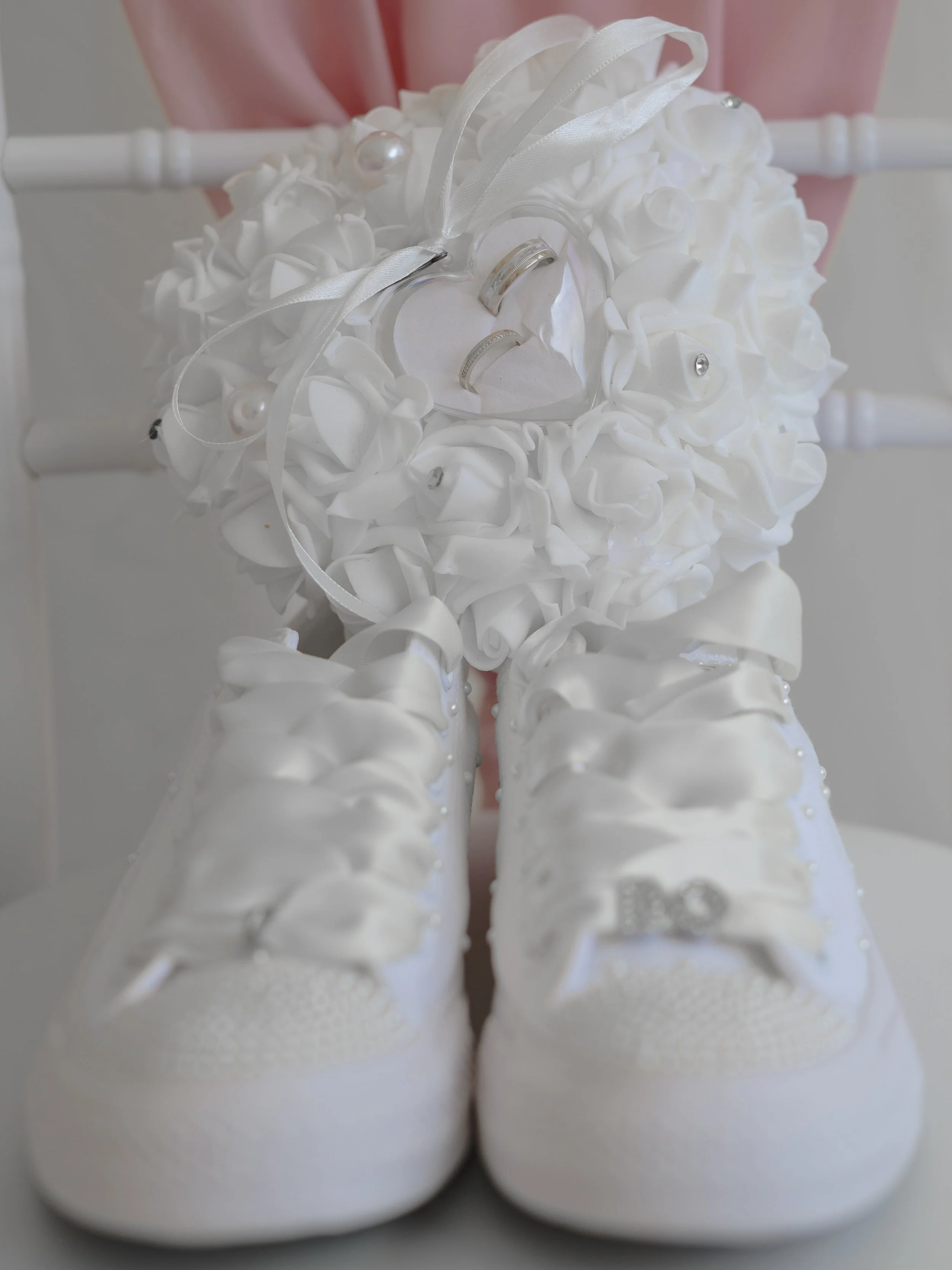 A pair of white ice skates with decorative white roses, ribbons, and rhinestones, used as a bridal accessory or wedding decoration.