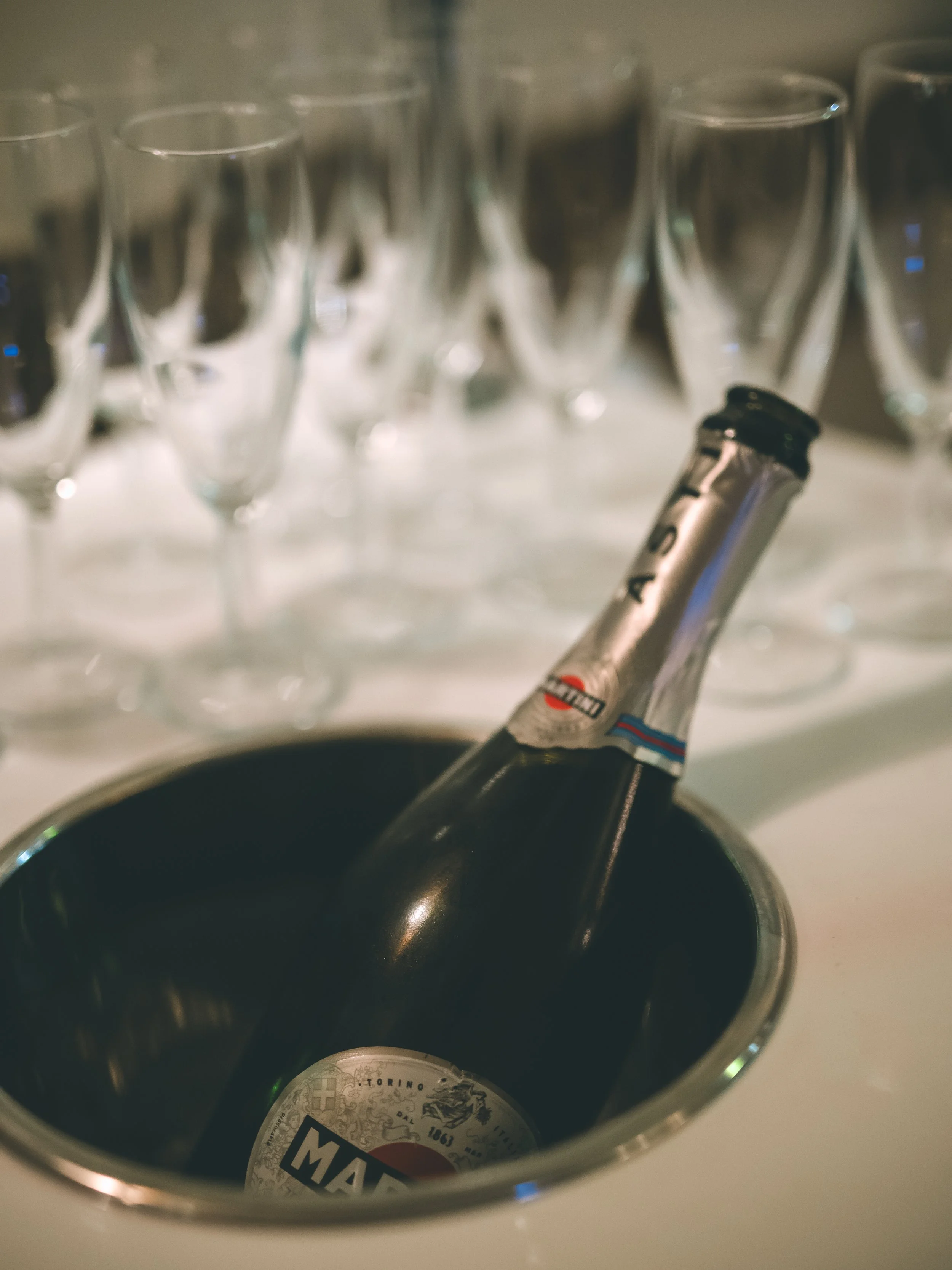 Shot of several empty glasses in the background and a focus on the inside of a metallic container with a bottle of Merlot wine.