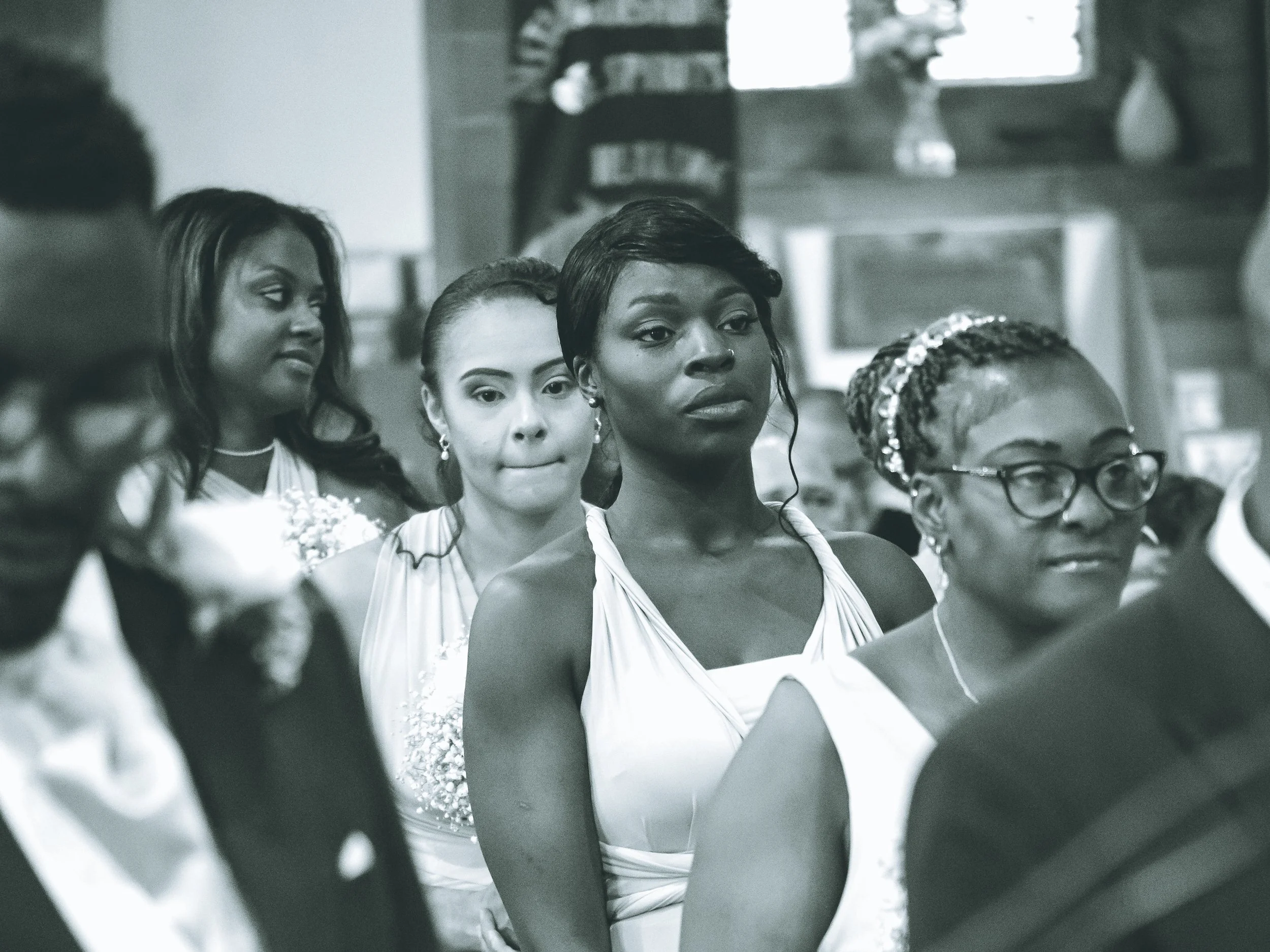 A group of women dressed in elegant white dresses, standing in a line during what appears to be a formal event or ceremony in an indoor setting.
