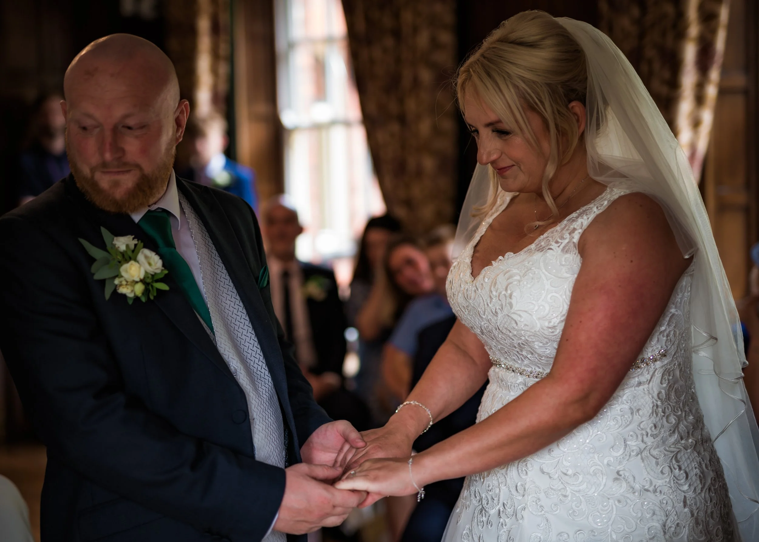 A bride and groom exchange wedding vows and hold hands inside a rustic wooden venue, with guests seated in the background.