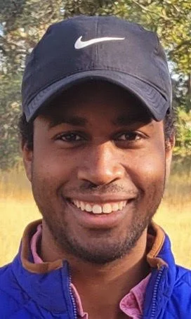 Close-up photo of a smiling man wearing a navy Nike cap and a blue jacket outdoors.