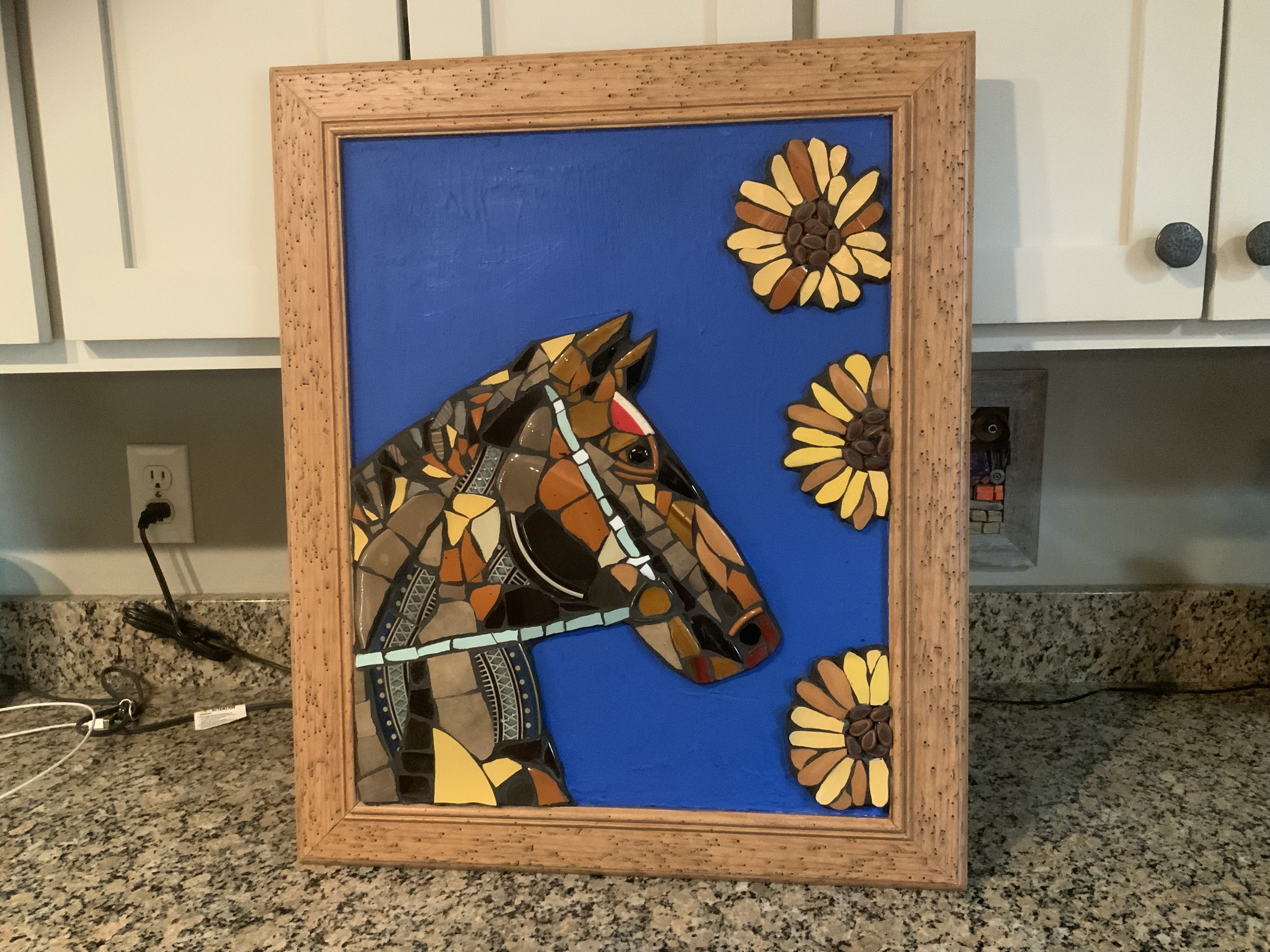 Mosaic artwork of a horse's head with three sunflowers against a blue background, framed in wood.