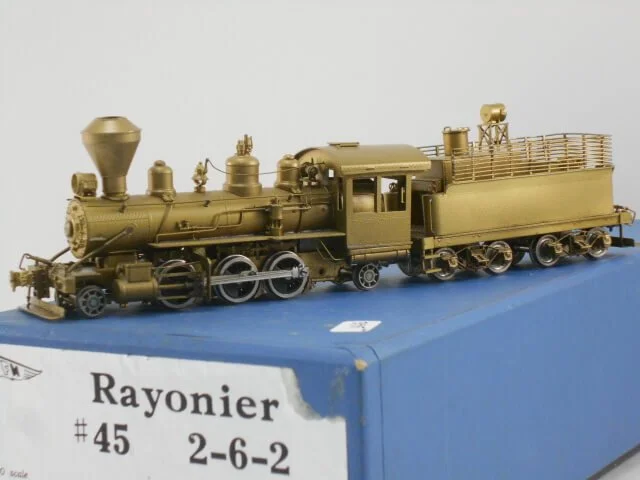 A detailed gold-colored model steam locomotive placed on a blue display box labeled 'Rayonier #45 2-6-2'.