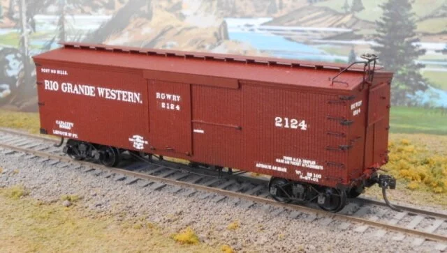 Model train boxcar on railway track with scenic background.
