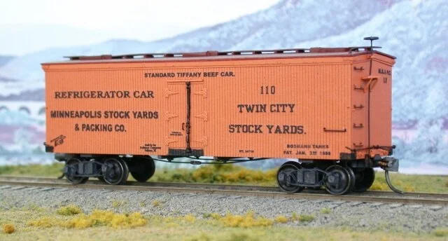 Orange vintage refrigerator train car on tracks with a snowy mountain backdrop.