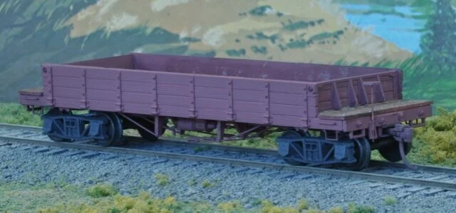 Model purple freight train car on tracks with a painted mountain background.