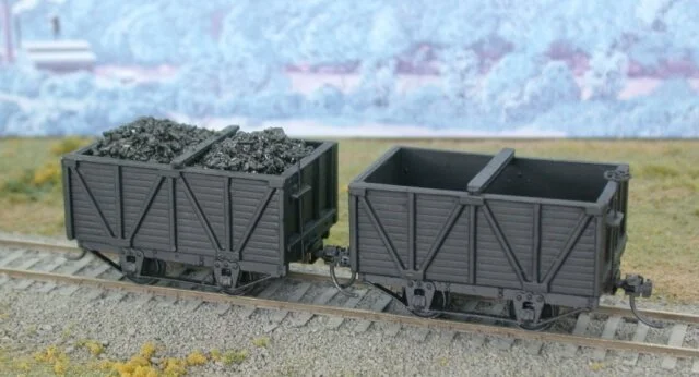 Model train cars on tracks, one filled with black coal and the other empty.