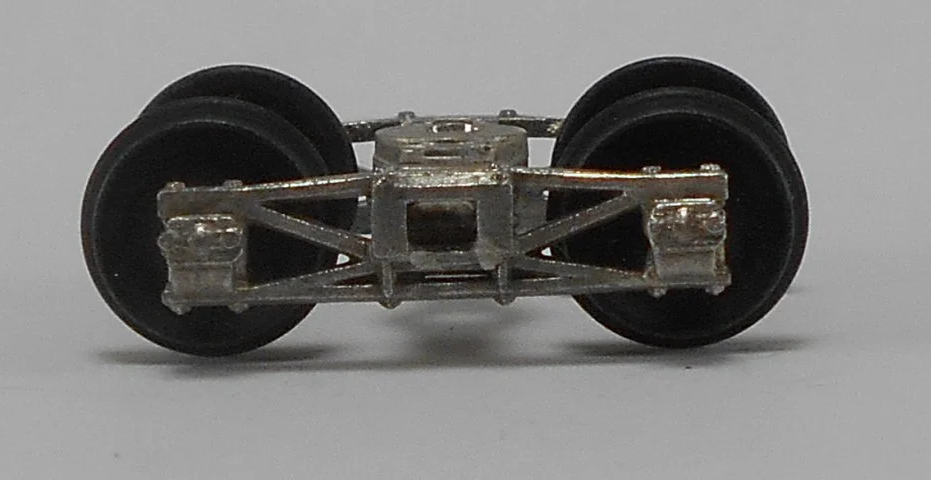 Close-up of a model train wheel assembly with metal framework and two black rubber wheels.