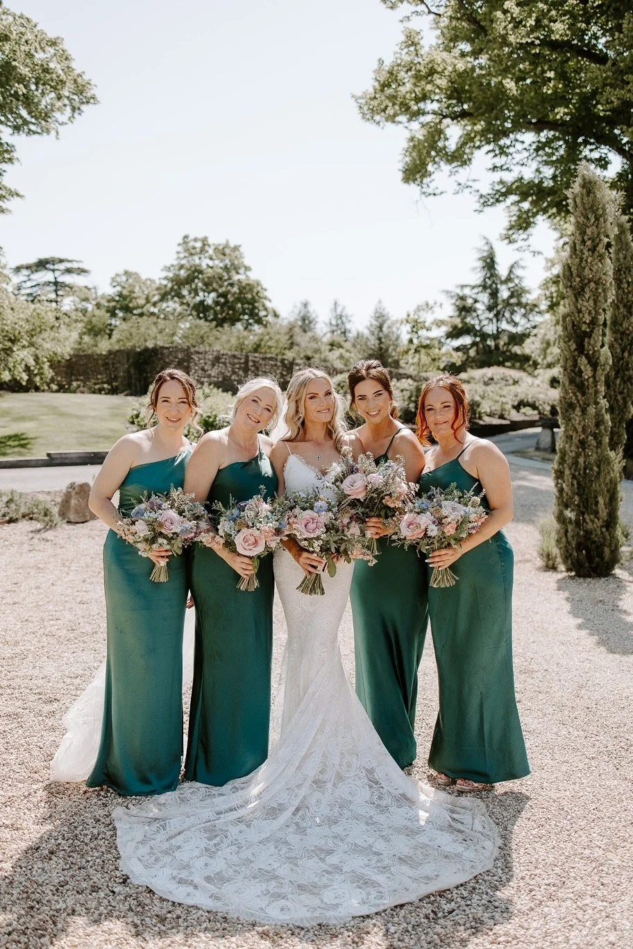a bride and her bridesmaids at wasing park on her wedding day- they are all holding beautiful bouquets of flowers