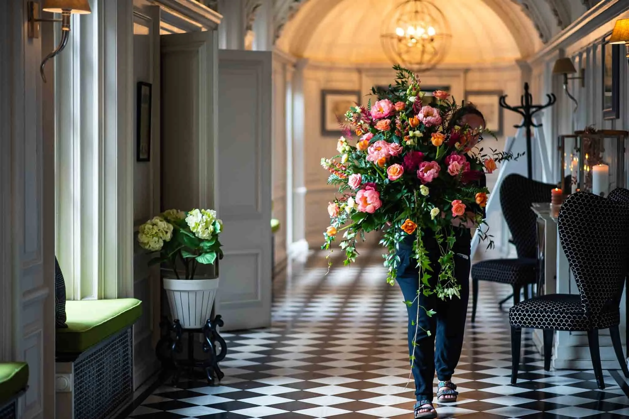 a florist moving wedding flowers over from ceremony to reception. she is mainly obscured by the large display she is holding at a lovely classic wedding venue.