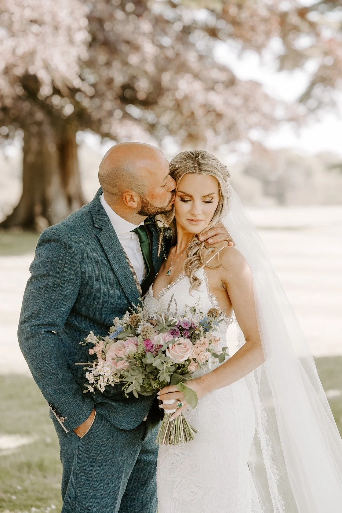 a bride and groom kissing aftertheir wedding at wasing park. the bride is holding a beautiful bouquet of pastel flowers