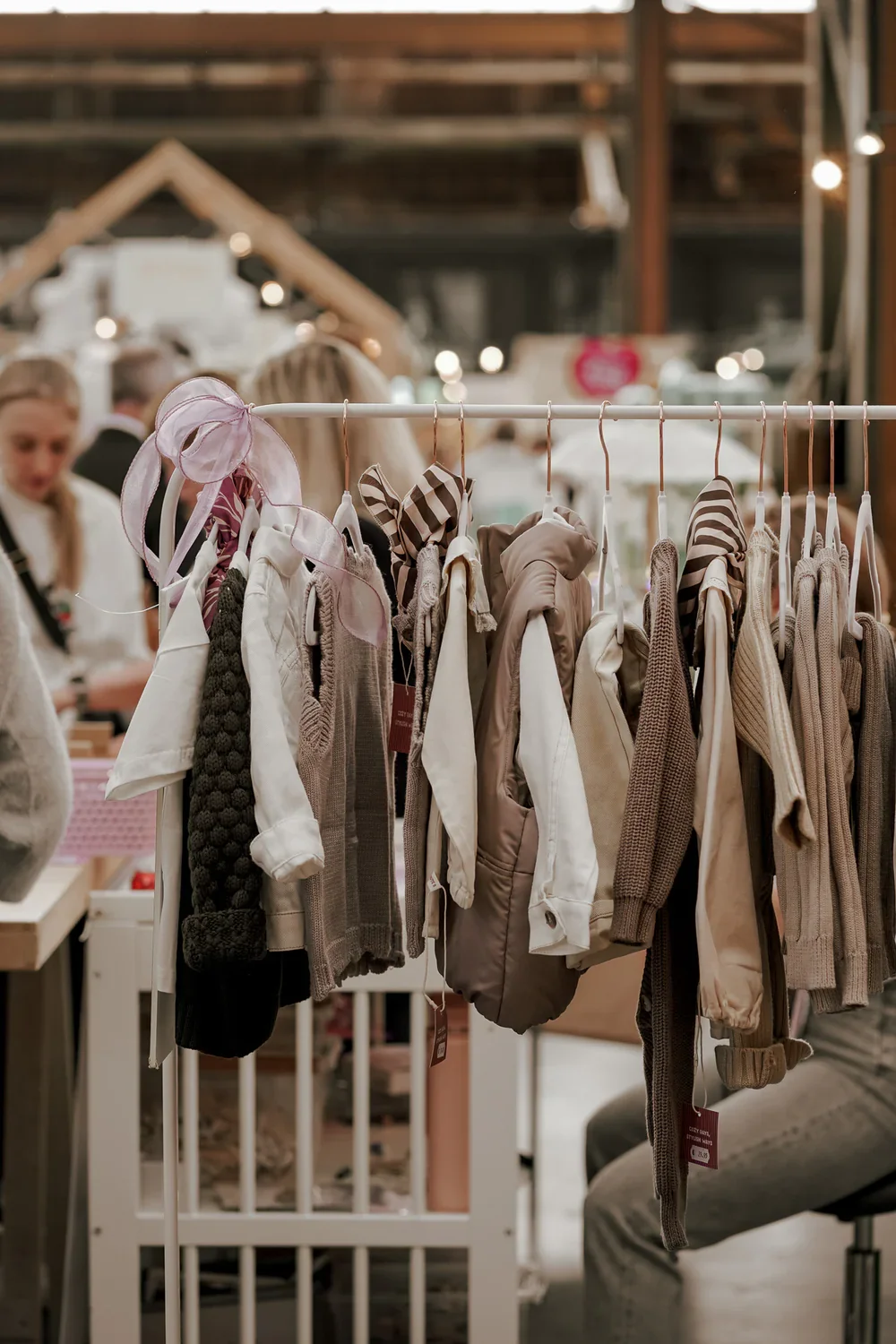 Babykleding hangt aan een kledingrek in een winkel, met mensen op de achtergrond.