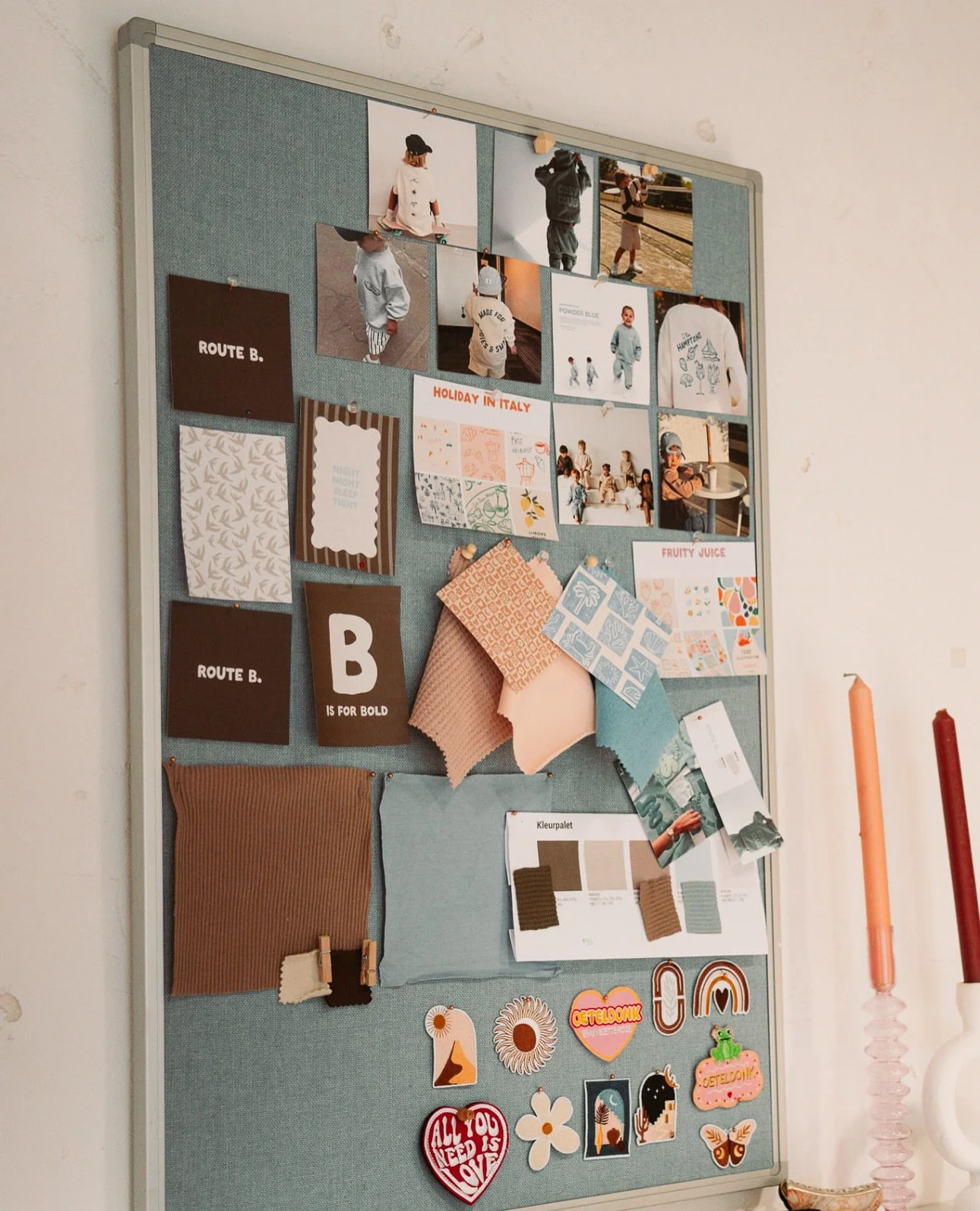 Een prikbord met foto's van kinderen, ontworpen stoffenstalen en decoratieve stickers.